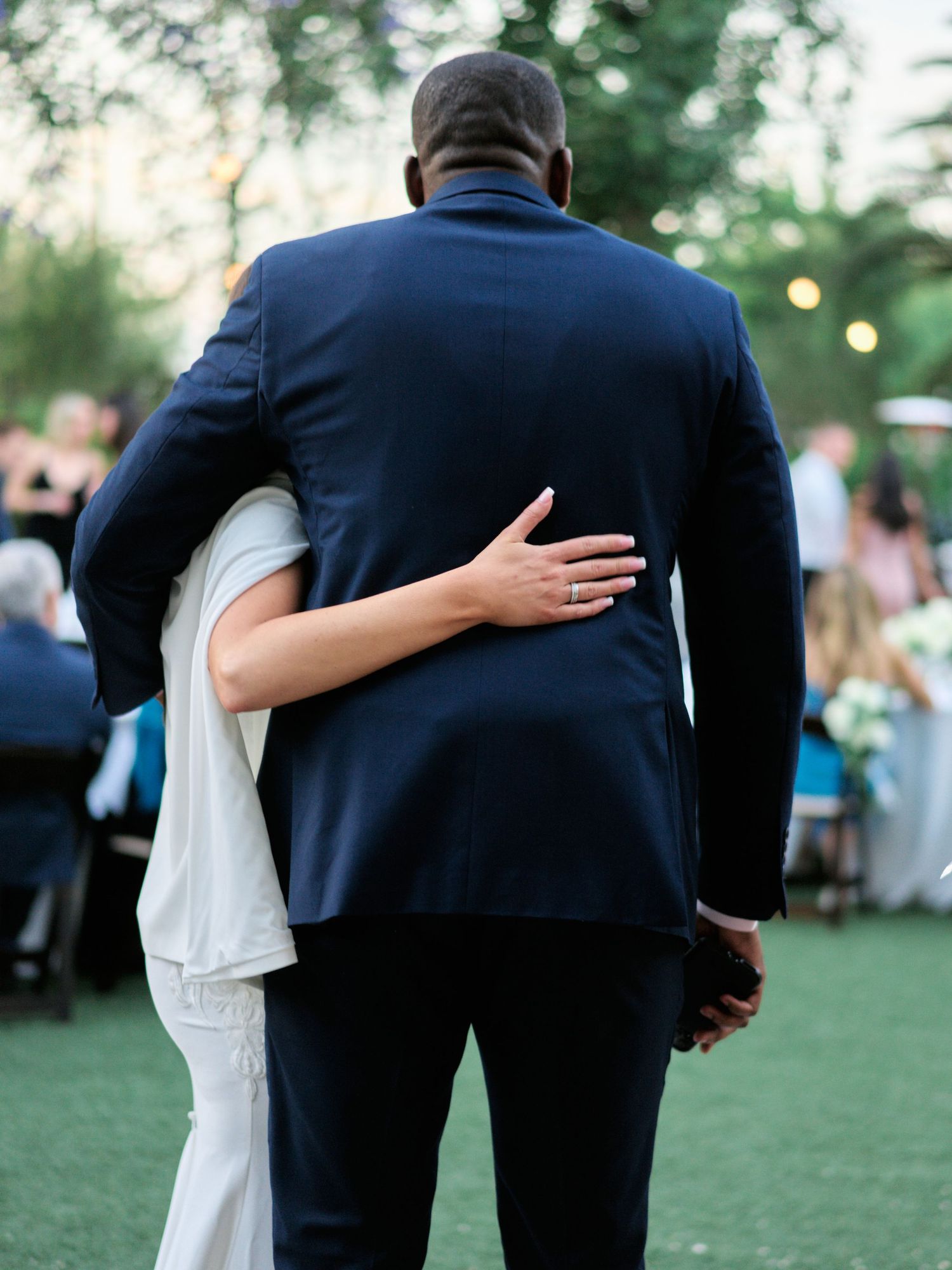 A tender embrace captured from behind during an outdoor wedding reception.