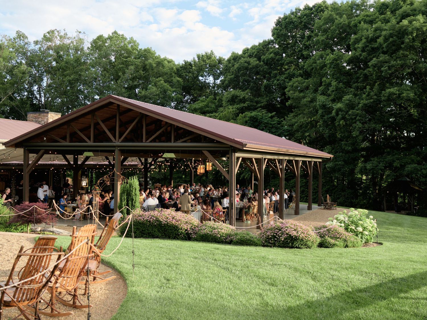 Rustic wooden pavilion surrounded by green lawn and trees for an outdoor event.