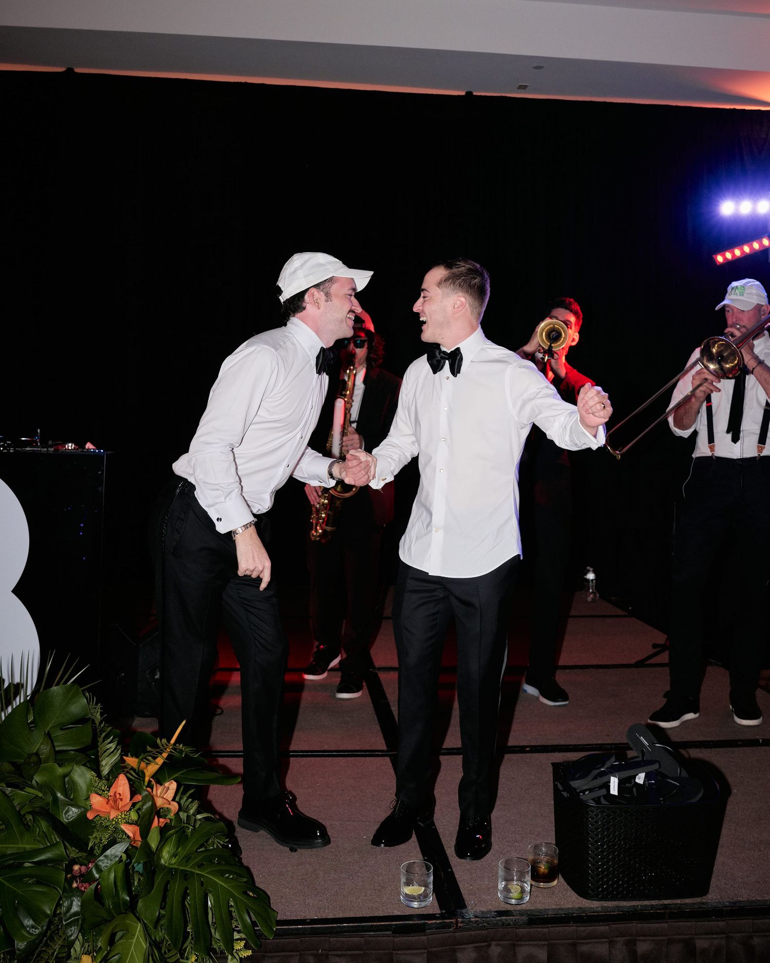 Two people in white formal attire dancing energetically together with musicians performing in the background.