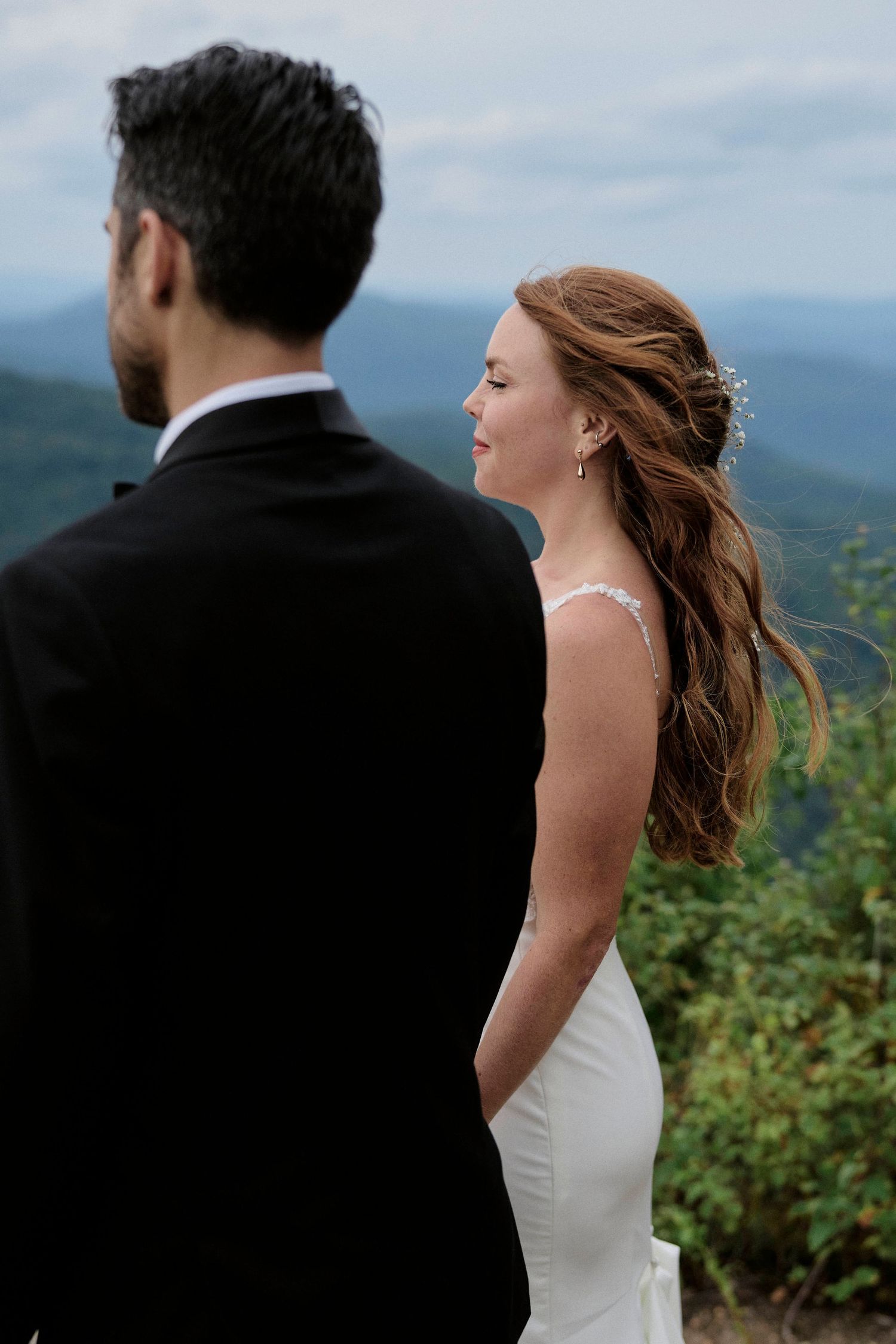 A couple enjoys a private moment on a mountain peak with rolling hills in the background.