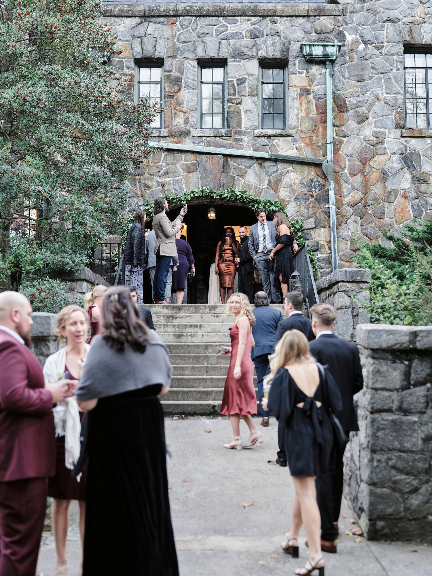 Elegantly dressed guests mingle on stone steps outside a historic building entrance.