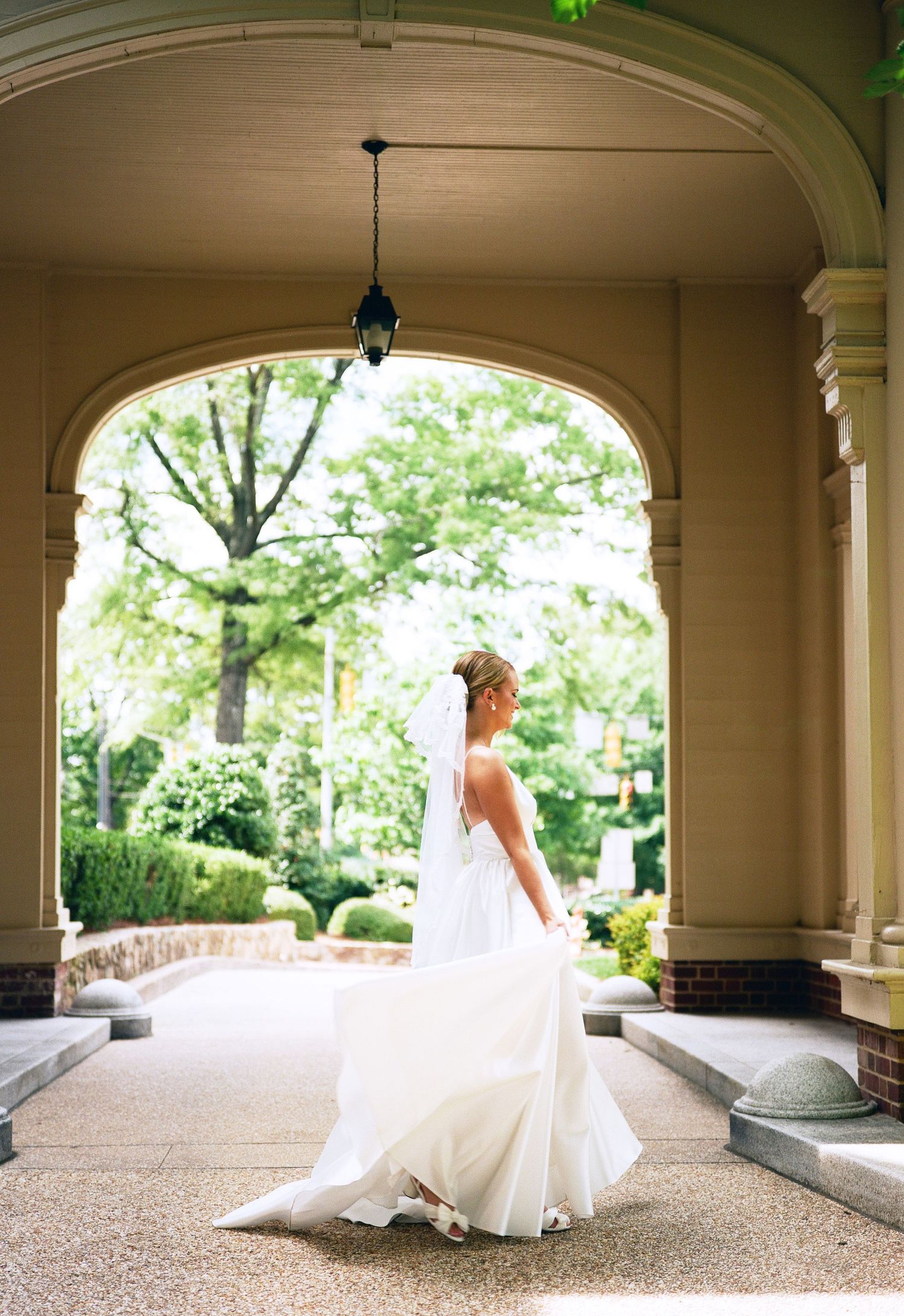 Ethereal bridal portrait under grand archway with flowing white dress and garden backdrop.