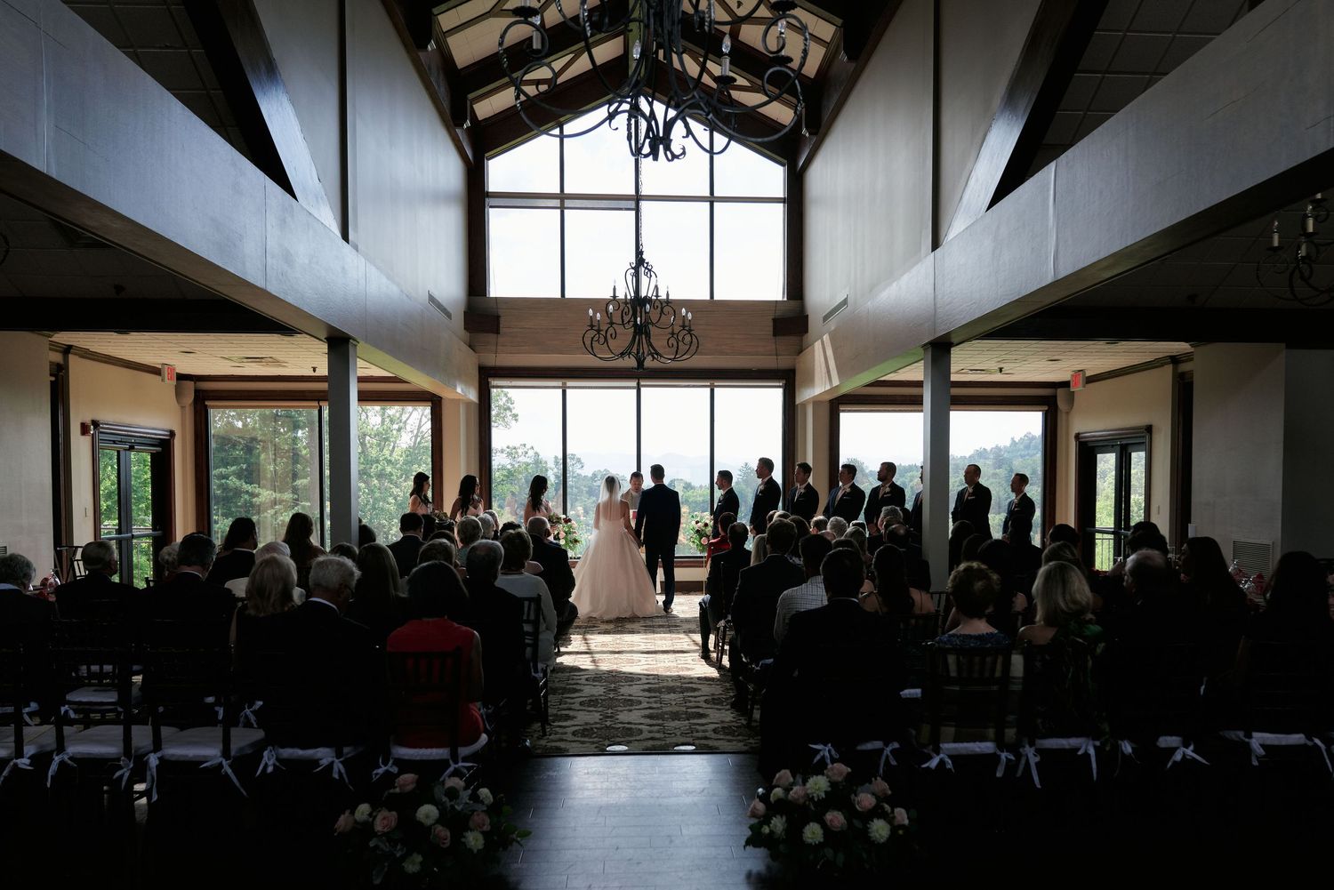 Wedding ceremony in progress at elegant venue with cathedral ceiling and backlit windows.