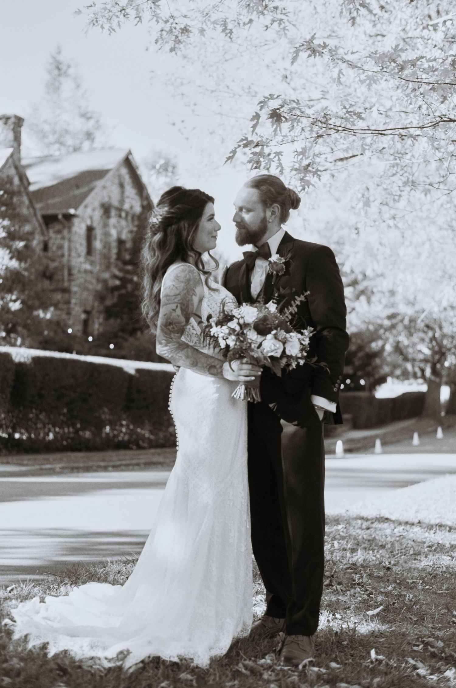 Black and white wedding portrait of couple with floral bouquet outdoors.
