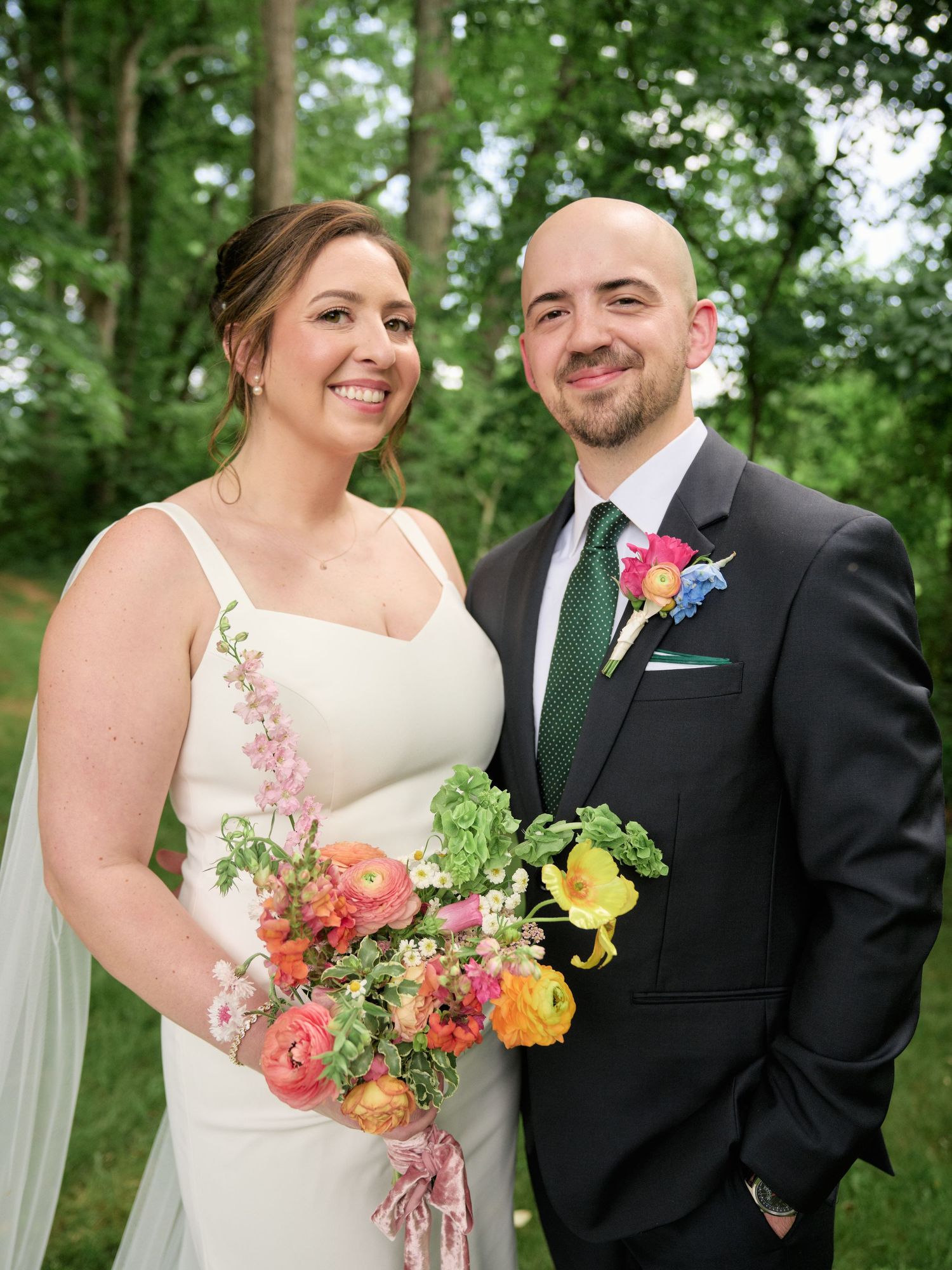 A joyful wedding portrait of a couple outdoors with the bride holding a vibrant spring bouquet.