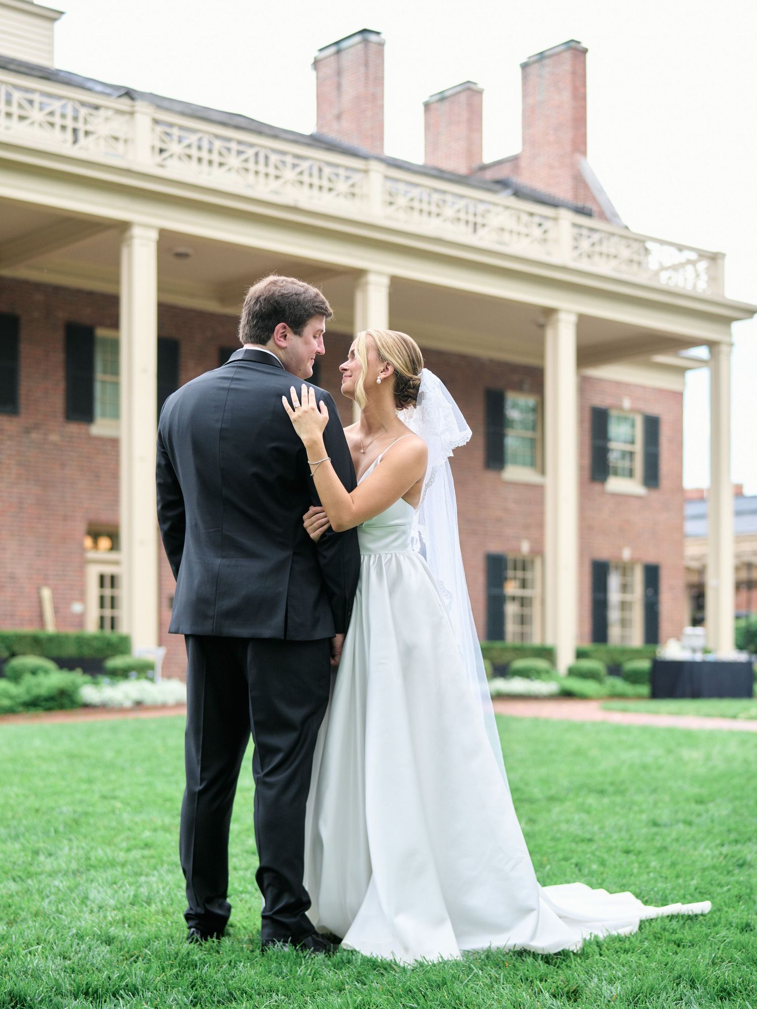 Tender moment between newlyweds on the lawn of an elegant brick estate.