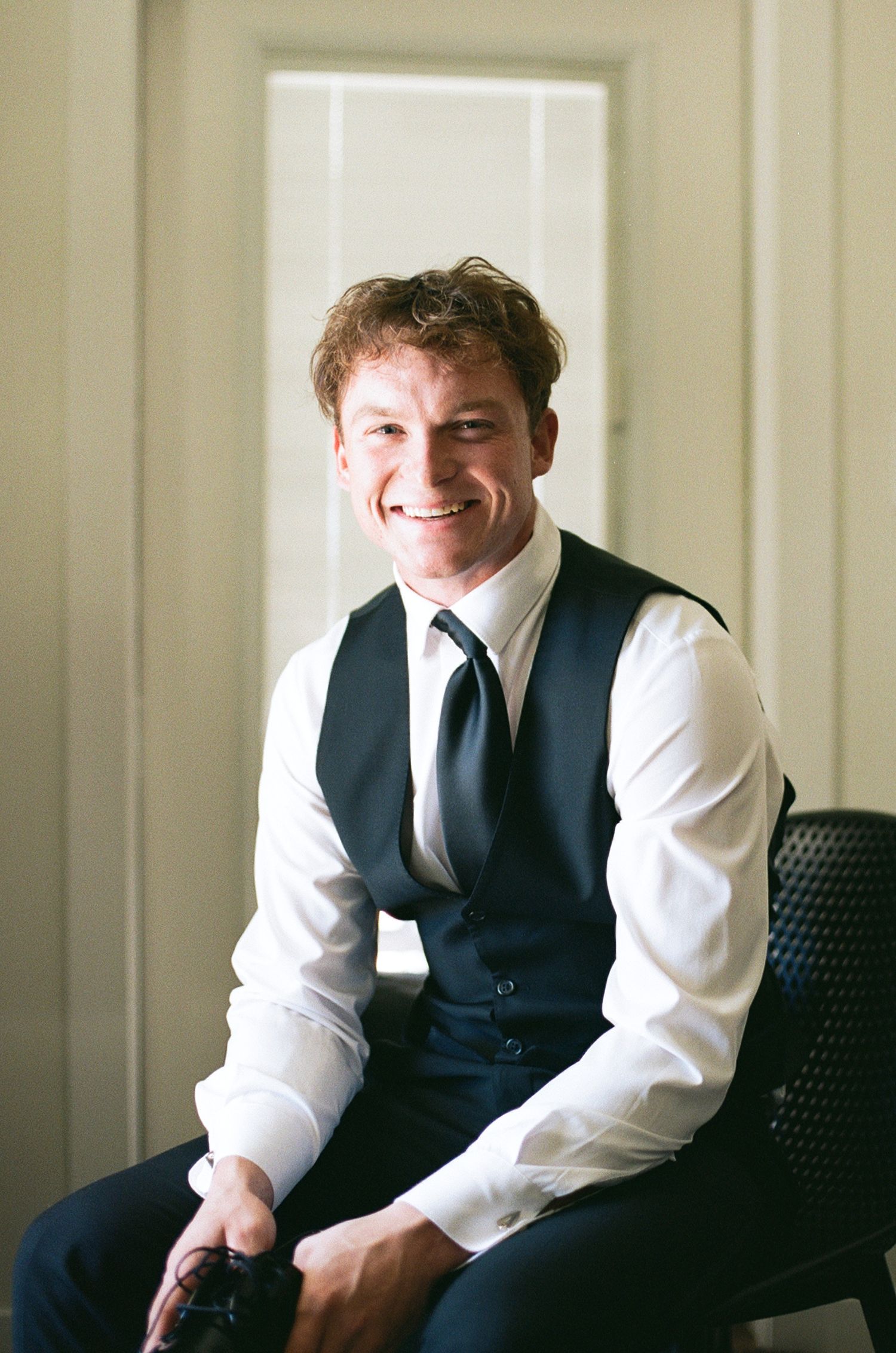 Professional portrait series showing a person in business attire seated on a black chair against a light colored wall.