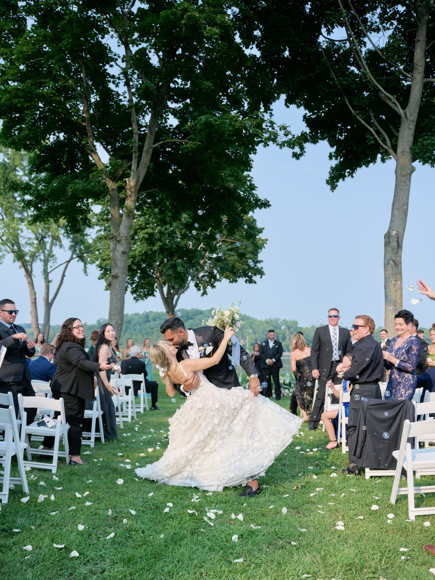 A bride and groom hold champagne flutes and smile at each other outdoors.