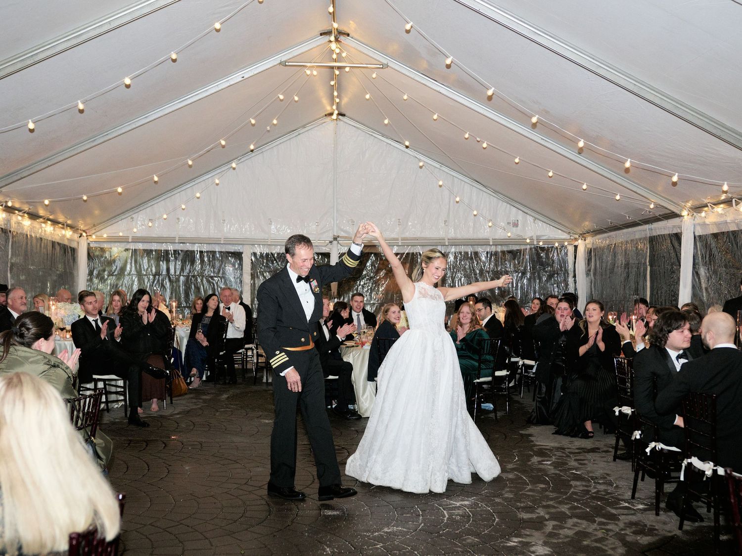 Bride and groom share first dance under elegant tent with string lights at romantic winter wedding reception.