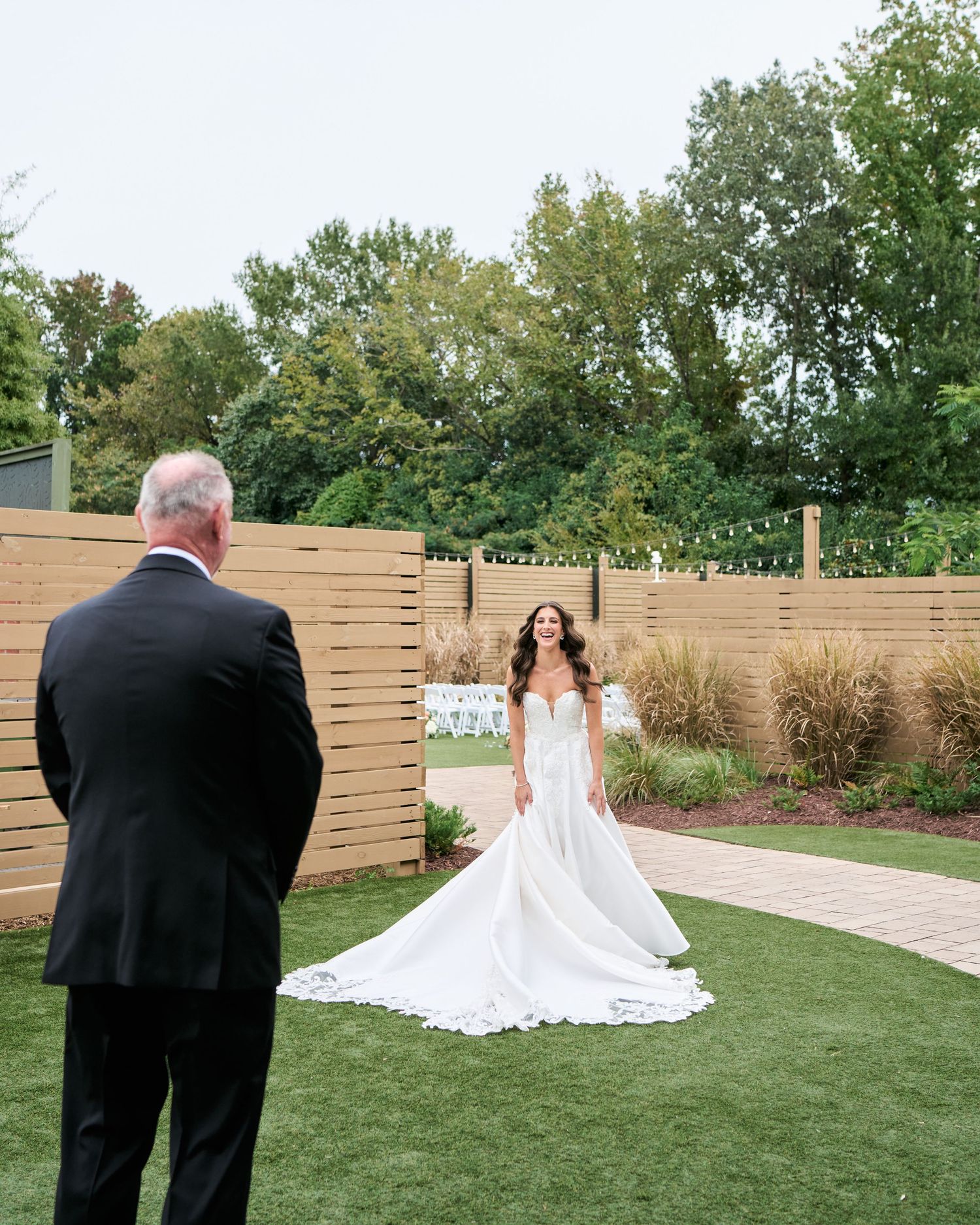 Bride in a white gown shares a first look moment with her father in an outdoor garden wedding venue.