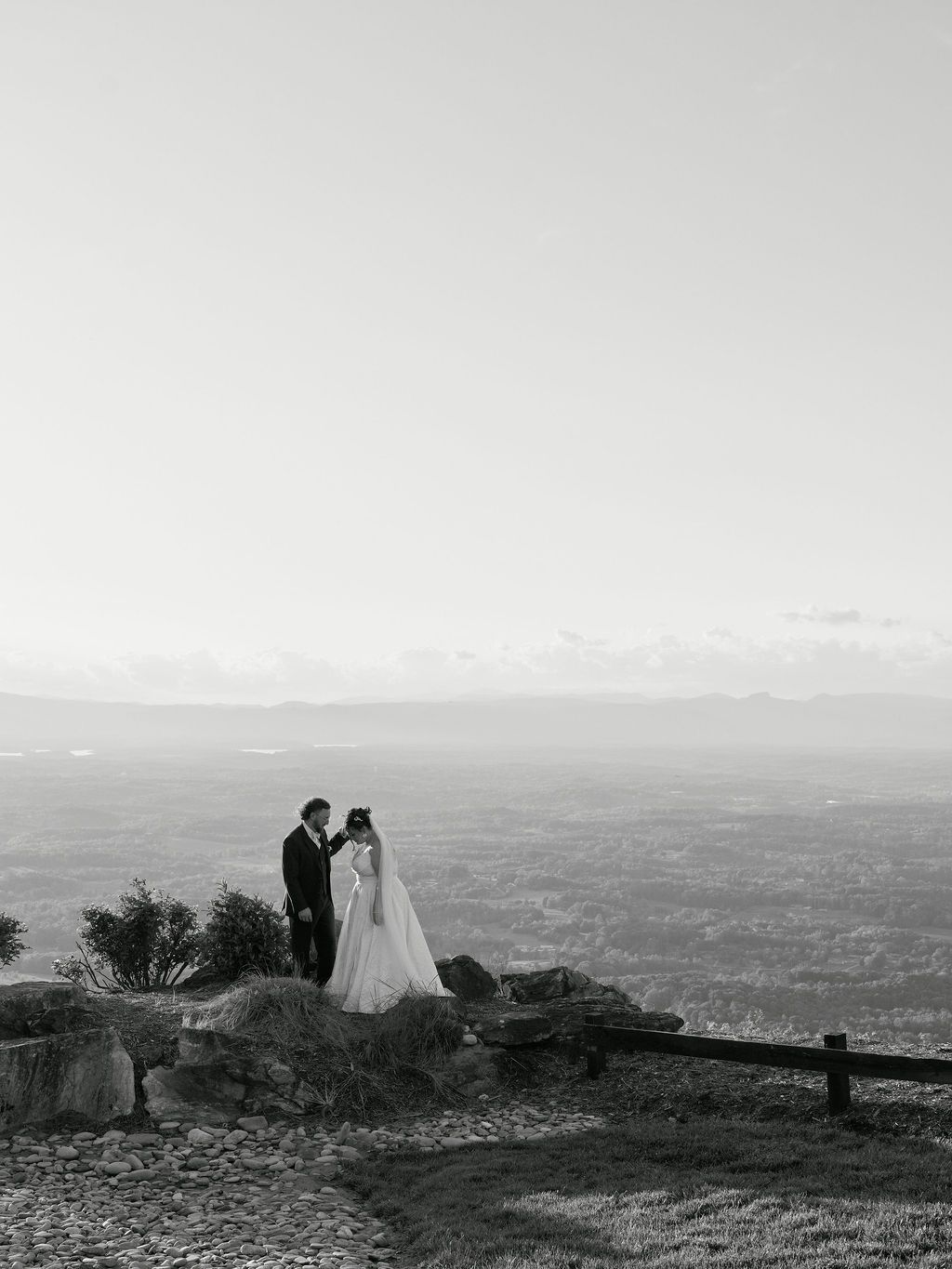 A romantic silhouette of a couple stands atop a scenic mountain overlook with panoramic views of the valley below.