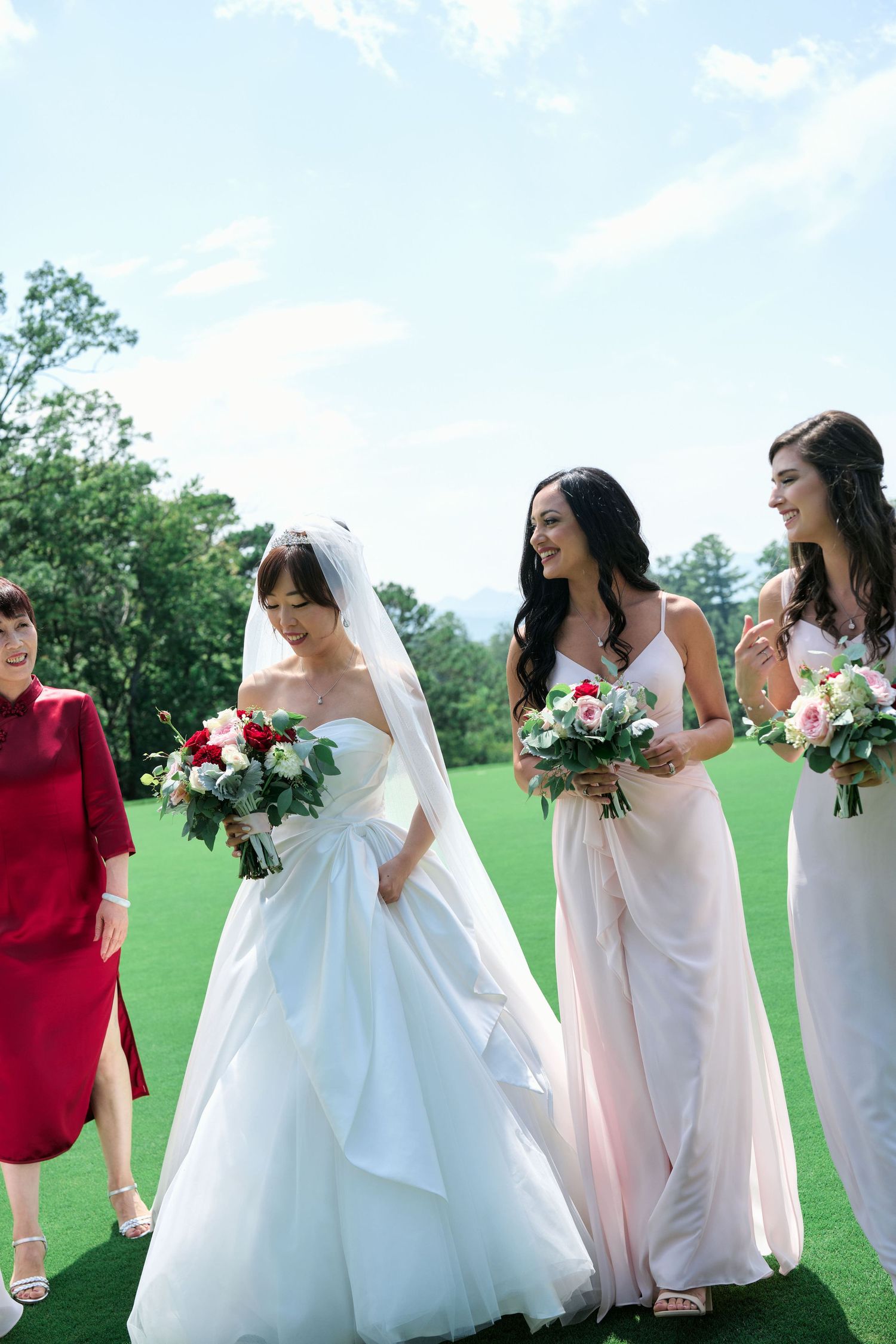Wedding party poses together on a golf course with bridesmaids in blush gowns holding floral bouquets.
