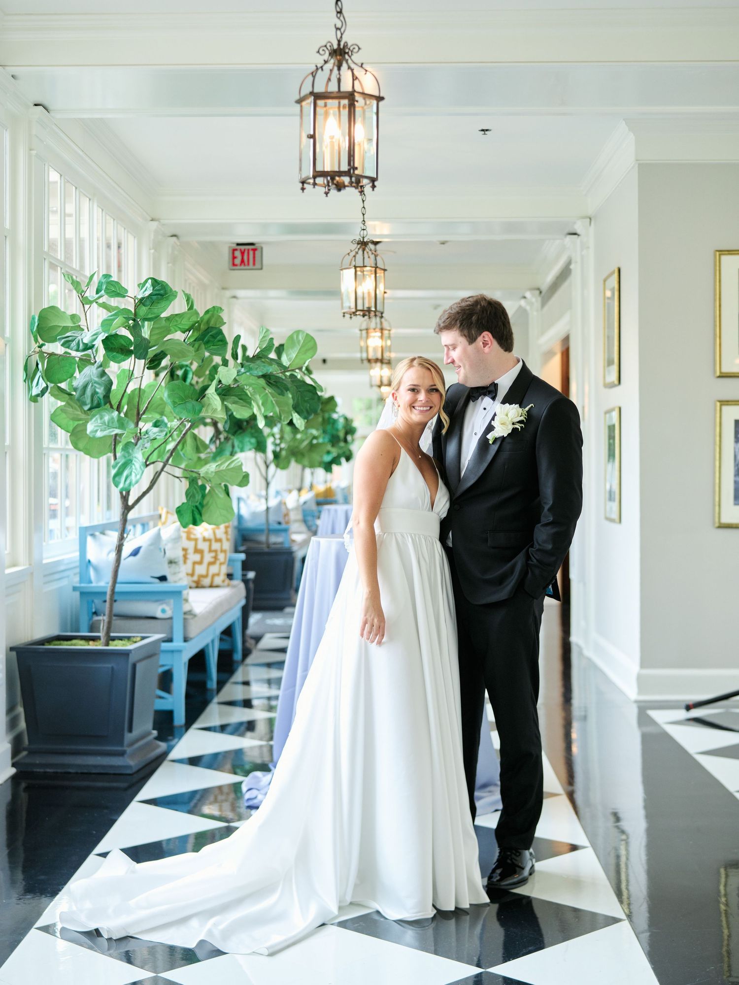 Bride and groom pose in elegant hallway with black and white floors and hanging lanterns.