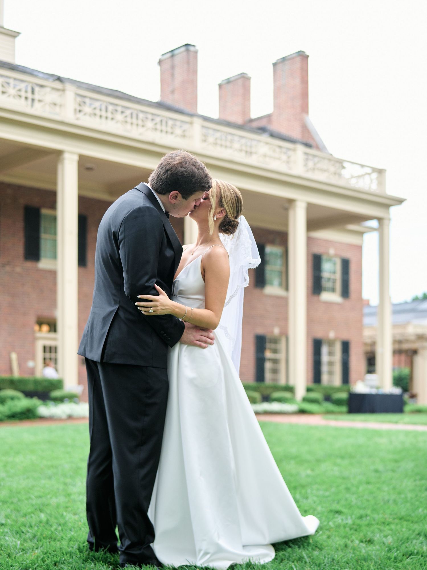 Romantic wedding moment captured in front of a historic brick building with white columns.
