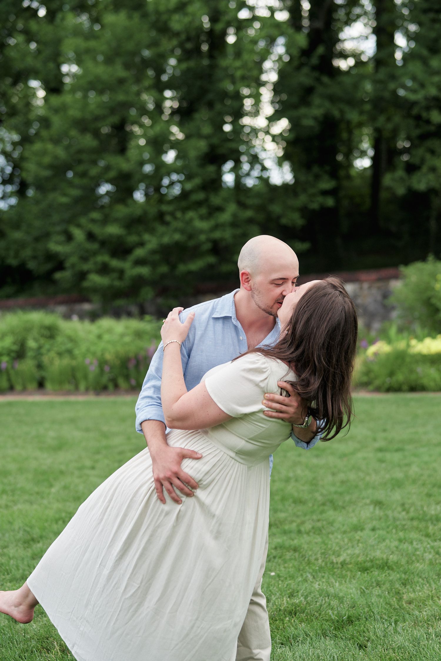 A romantic dip pose captured in a garden setting with trees in the background.