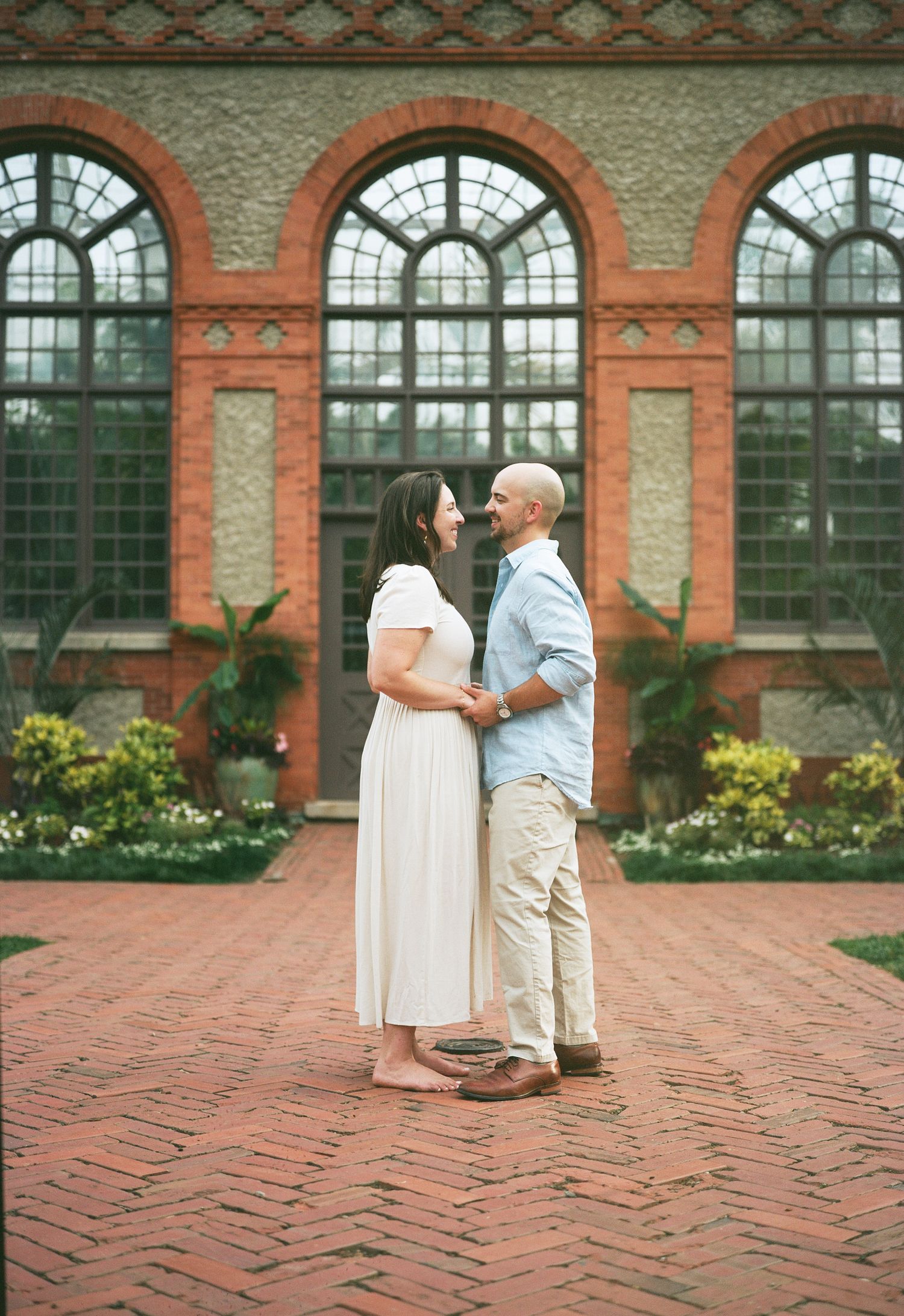 A couple embraces in front of ornate arched windows with red brick detailing.