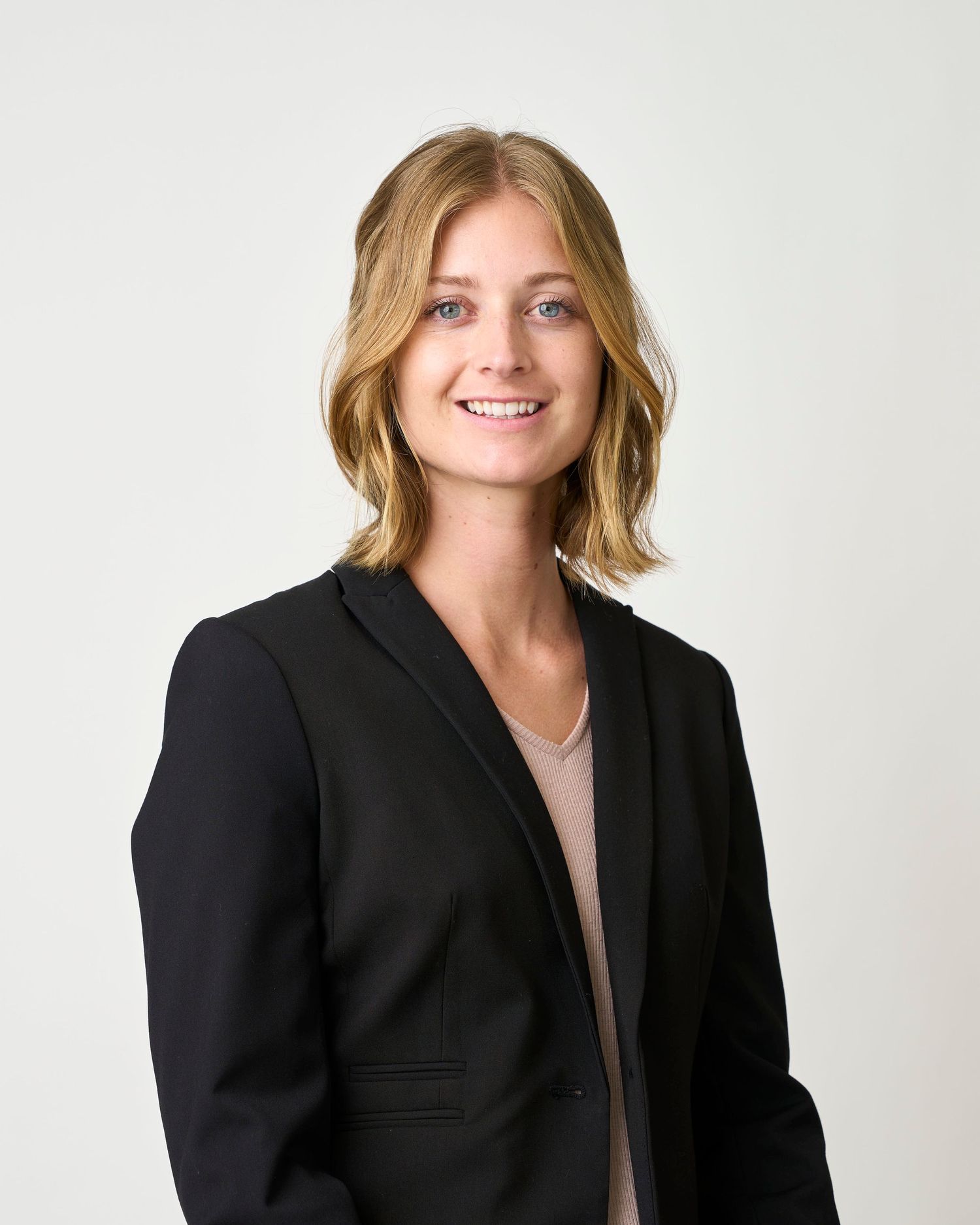 Professional headshot of a lady sitting in a studio in front of a white backdrop.