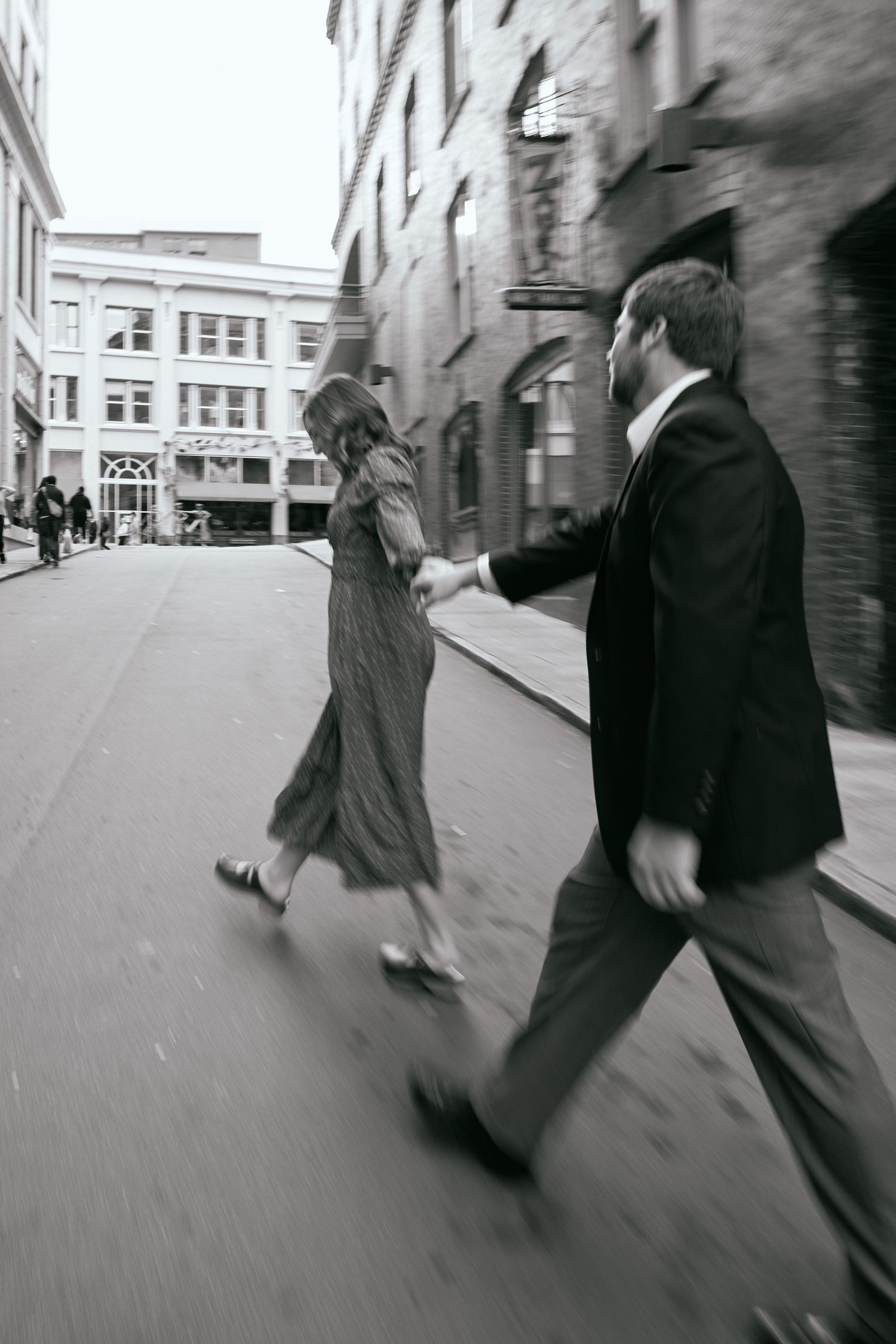 A couple walks down a city street in vintage-style black and white photography.