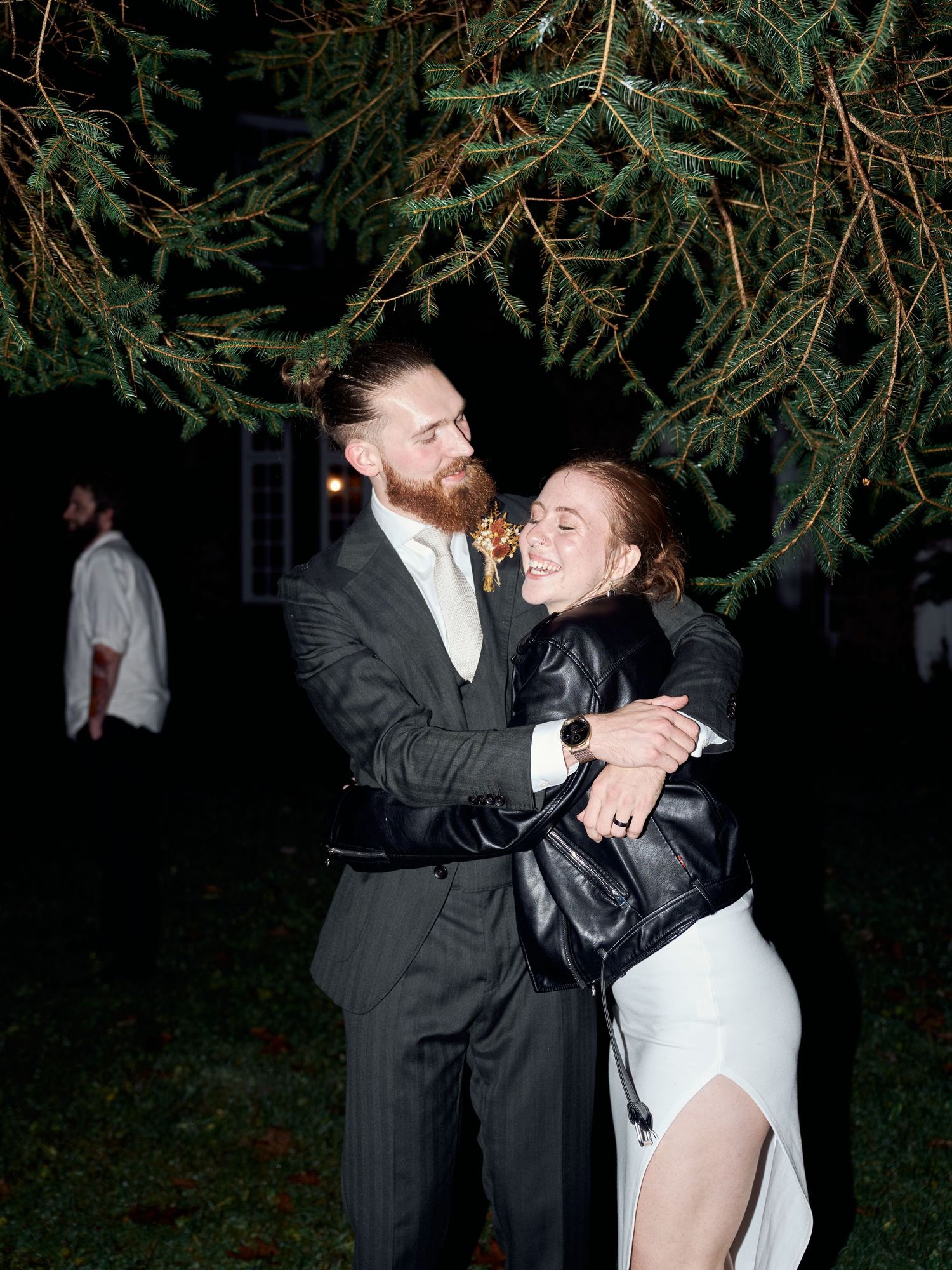 A couple embraces under pine tree branches at night during their wedding celebration.