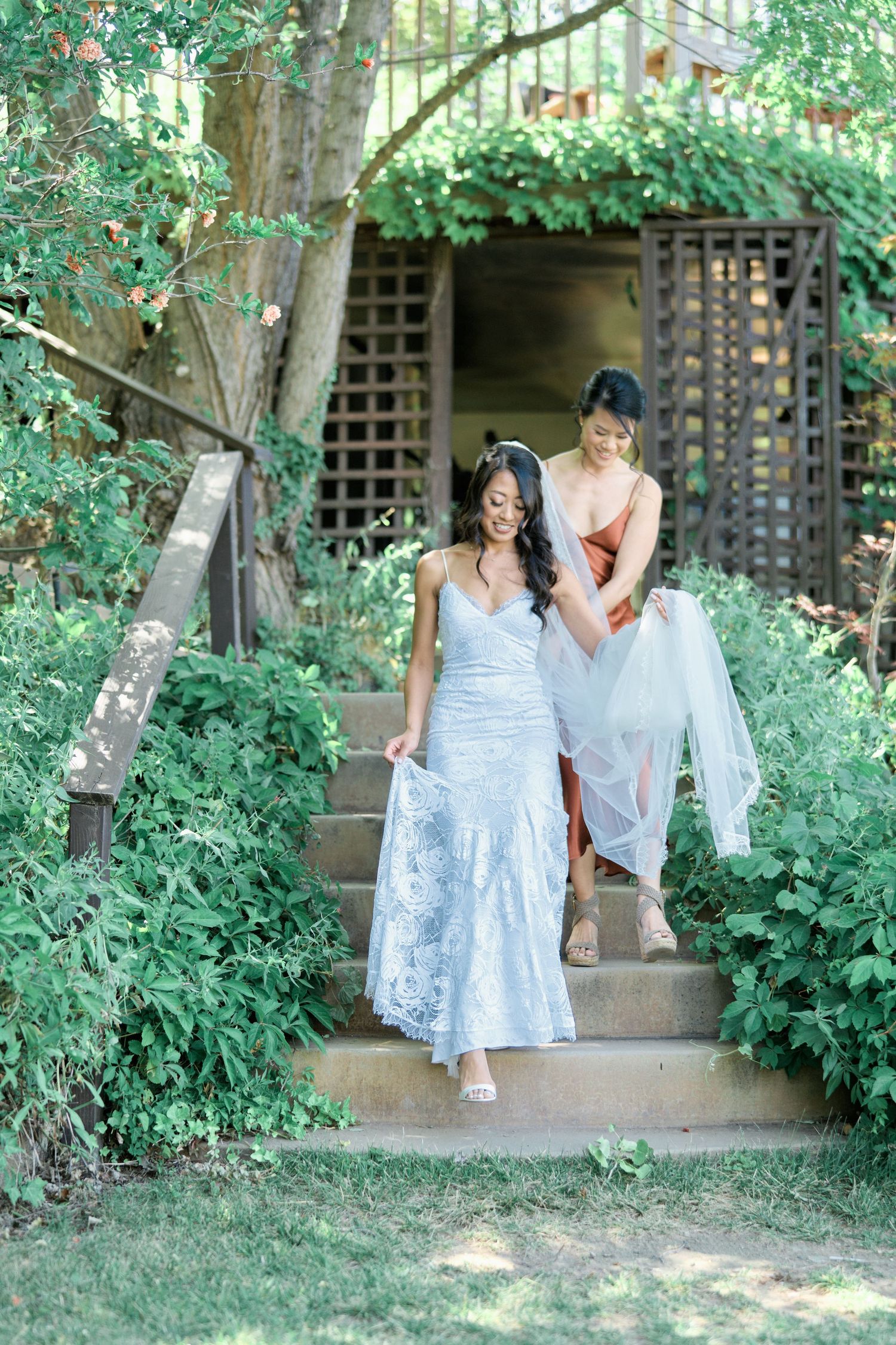 Two people in formal attire descending garden steps surrounded by lush greenery.