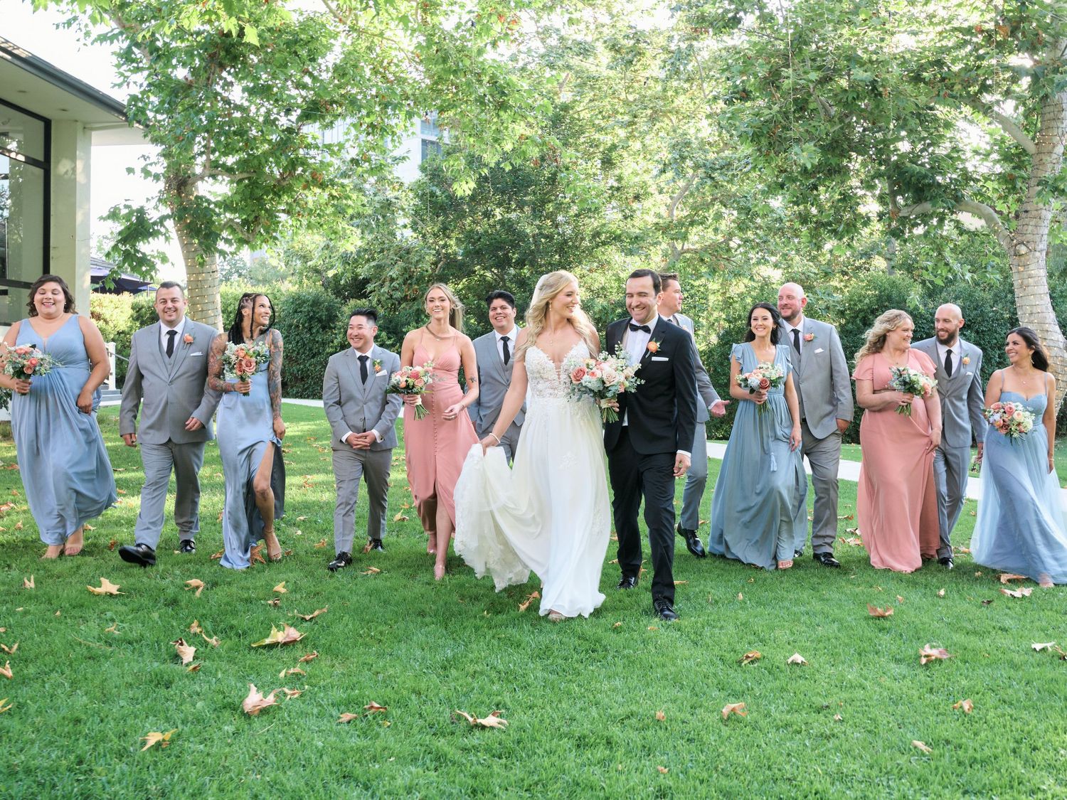 Wedding party walks across a green lawn wearing pink and blue attire.