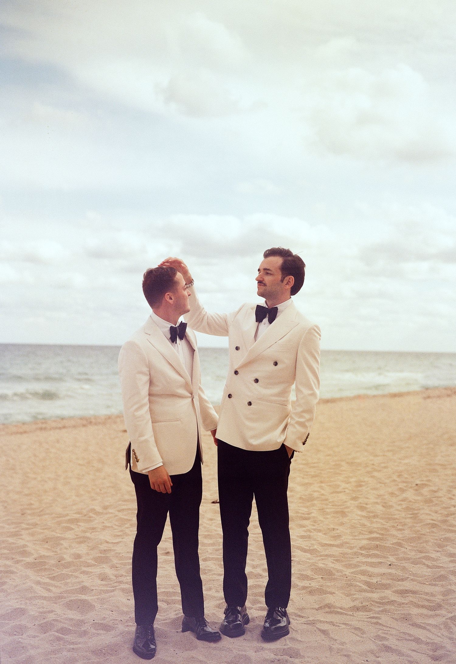 Two people in cream jackets share an intimate moment on a beach.
