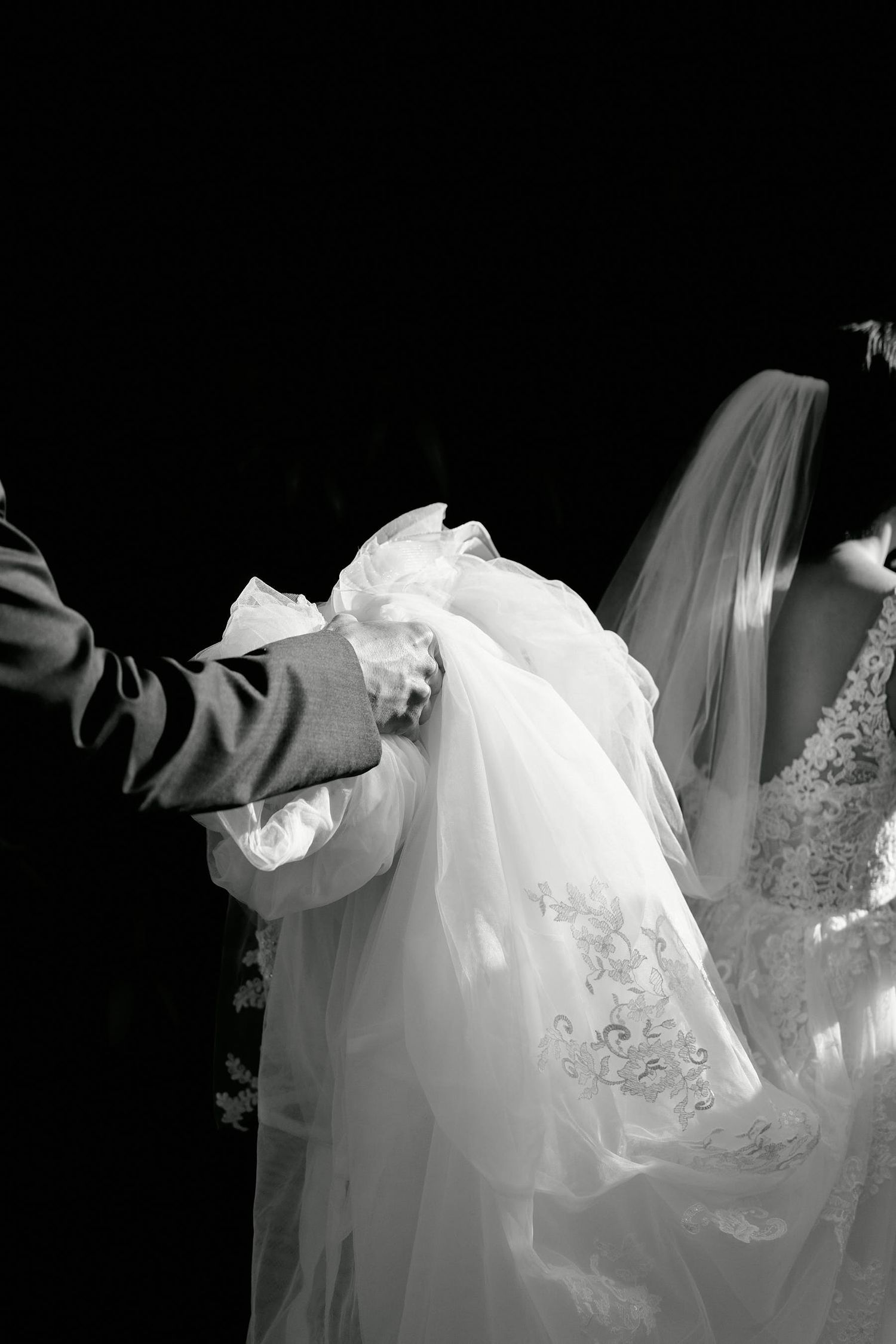 Black and white wedding photo showing delicate details of a bride's veil and dress during ceremony.