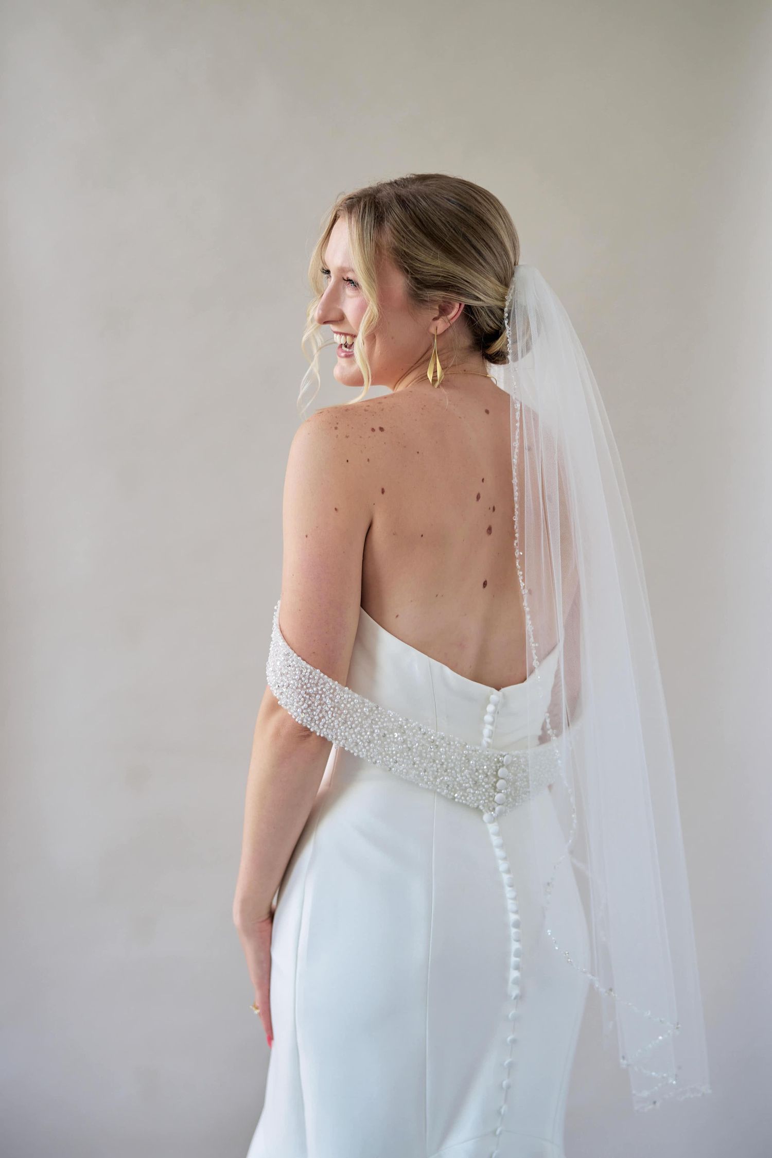 Back view of wedding dress showing intricate button detail and sheer veil against white wall.