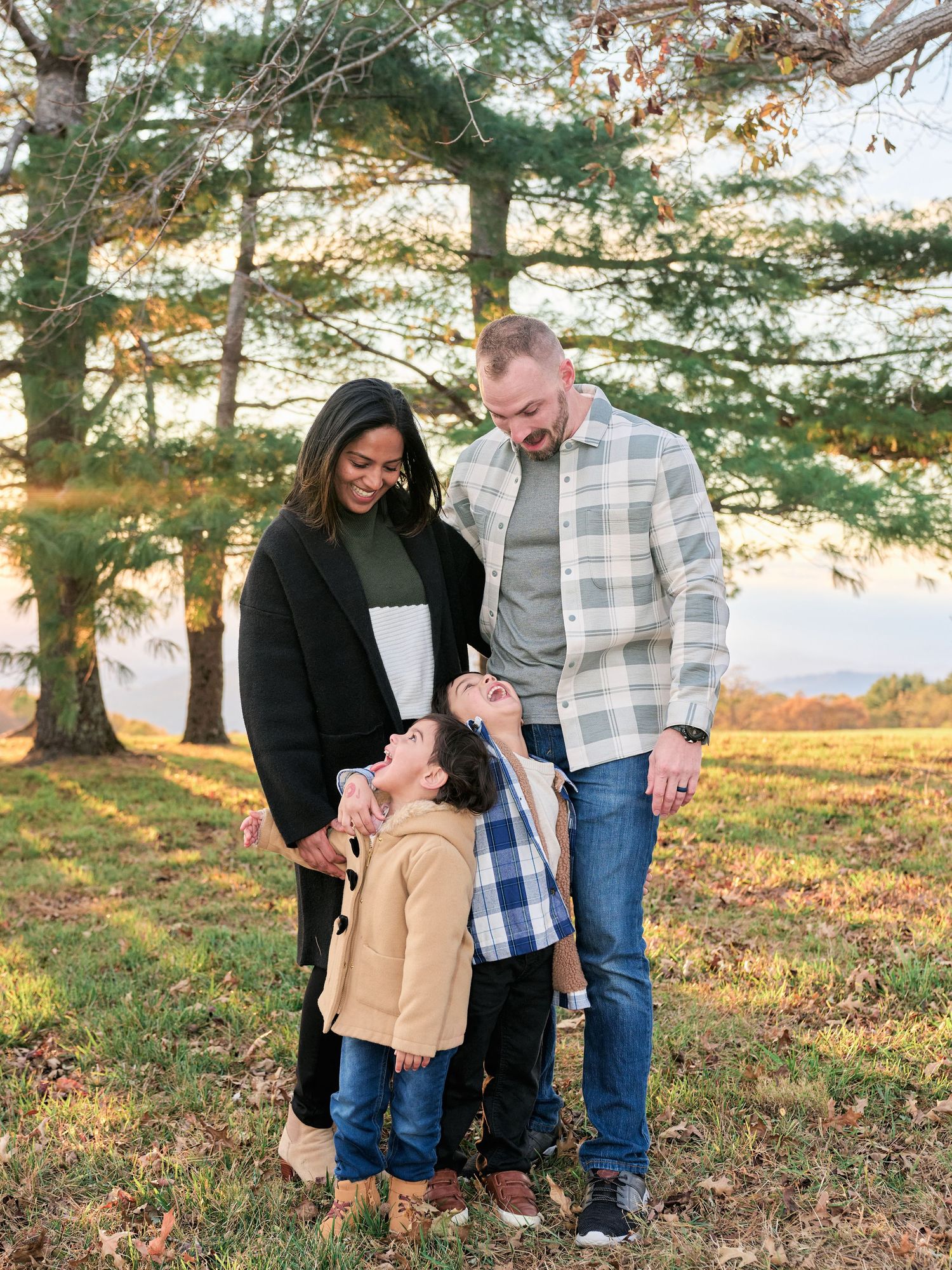 A family shares tender moments together while playing outdoors under tall trees during a golden autumn afternoon.