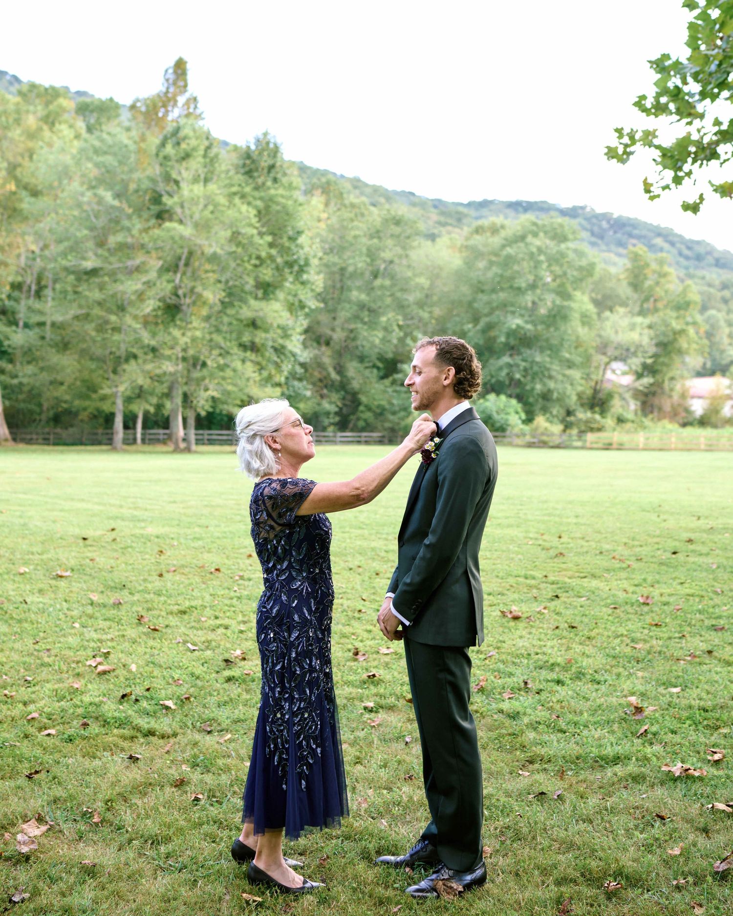 A couple shares a playful moment in a grassy field with mountains visible in the background.