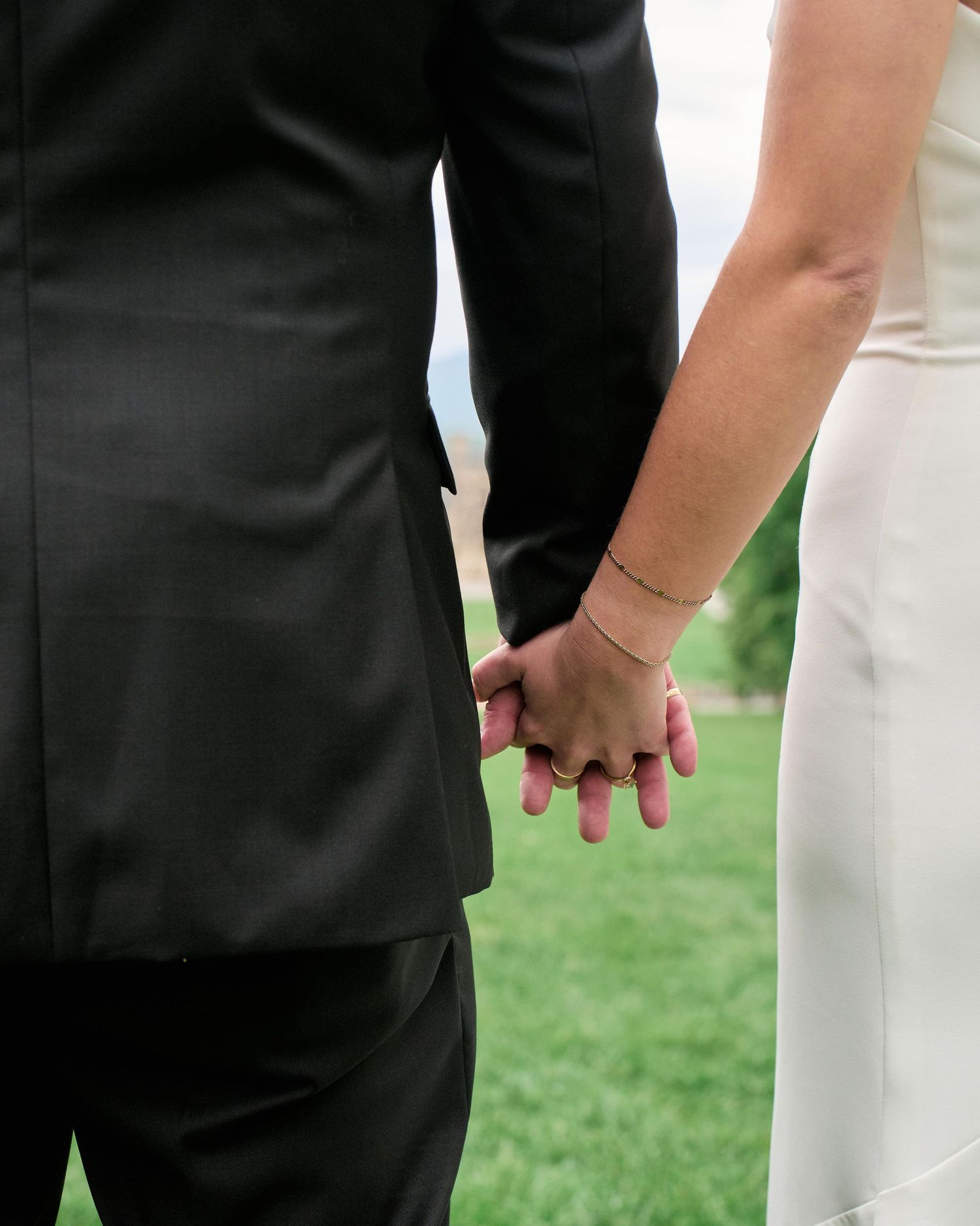 A close-up view of hands wearing formal attire, with one person in black and another in white, during a wedding ceremony.