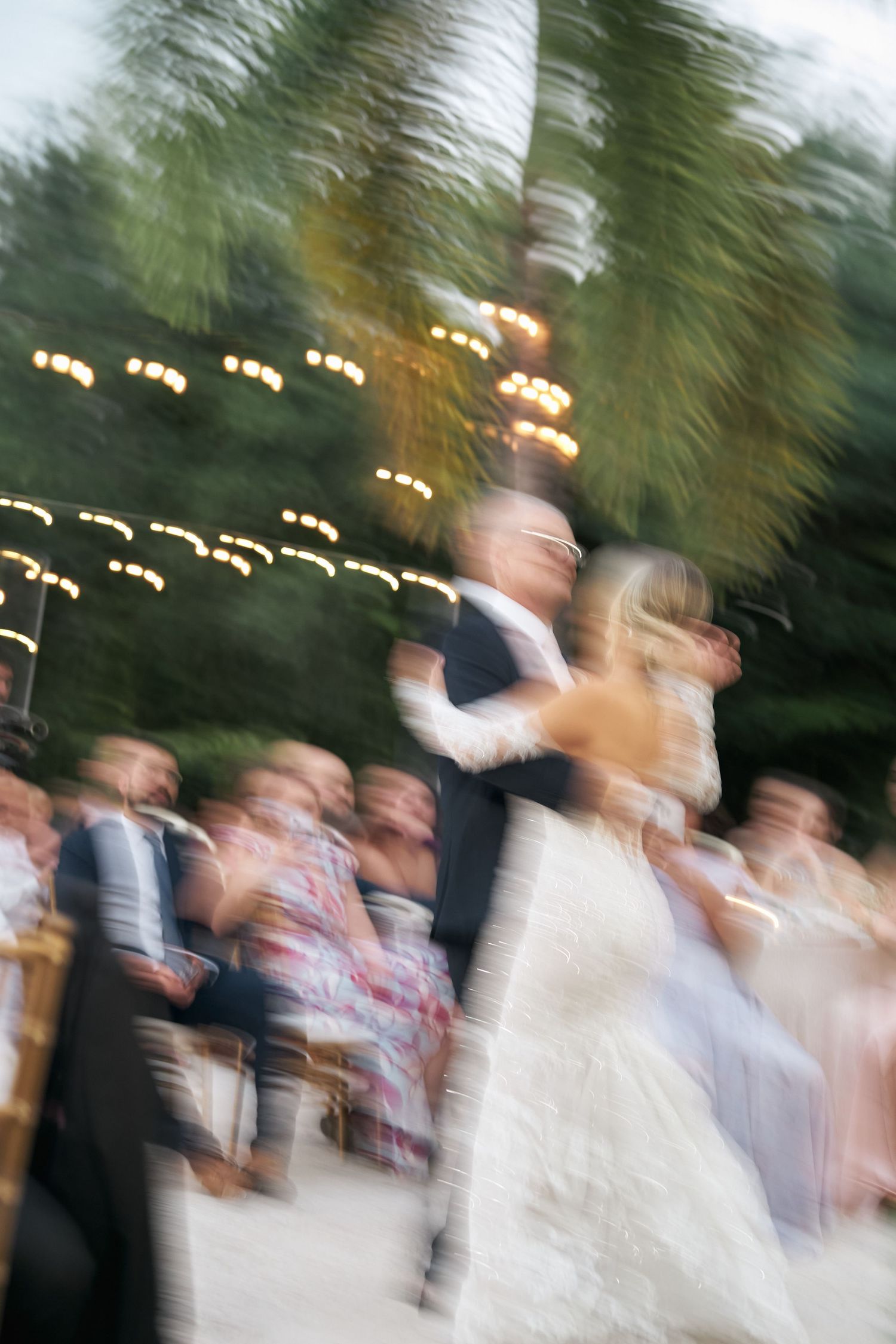 Motion blur wedding dance photo with string lights and guests creating a dreamy effect.
