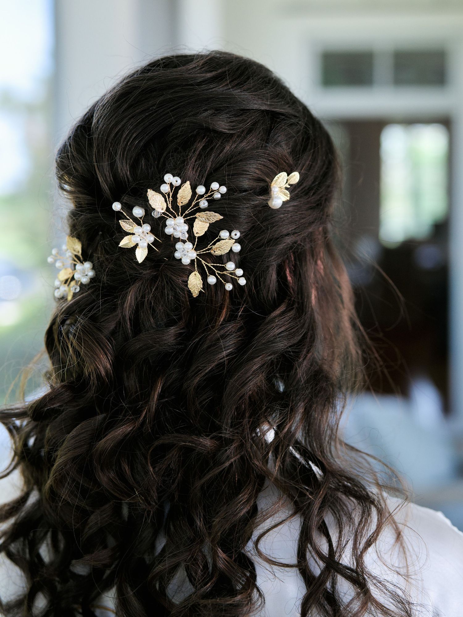 Delicate pearl and crystal hair accessories adororn dark wavy hair in an elegant half-up bridal hairstyle.