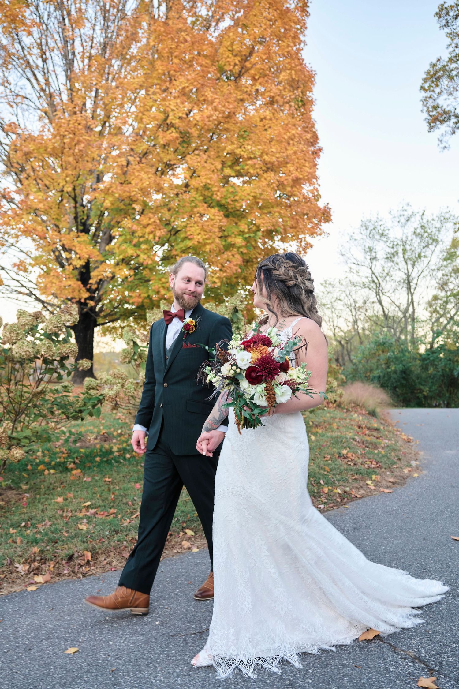 A couple walks along an autumn path with vibrant orange maple trees overhead.