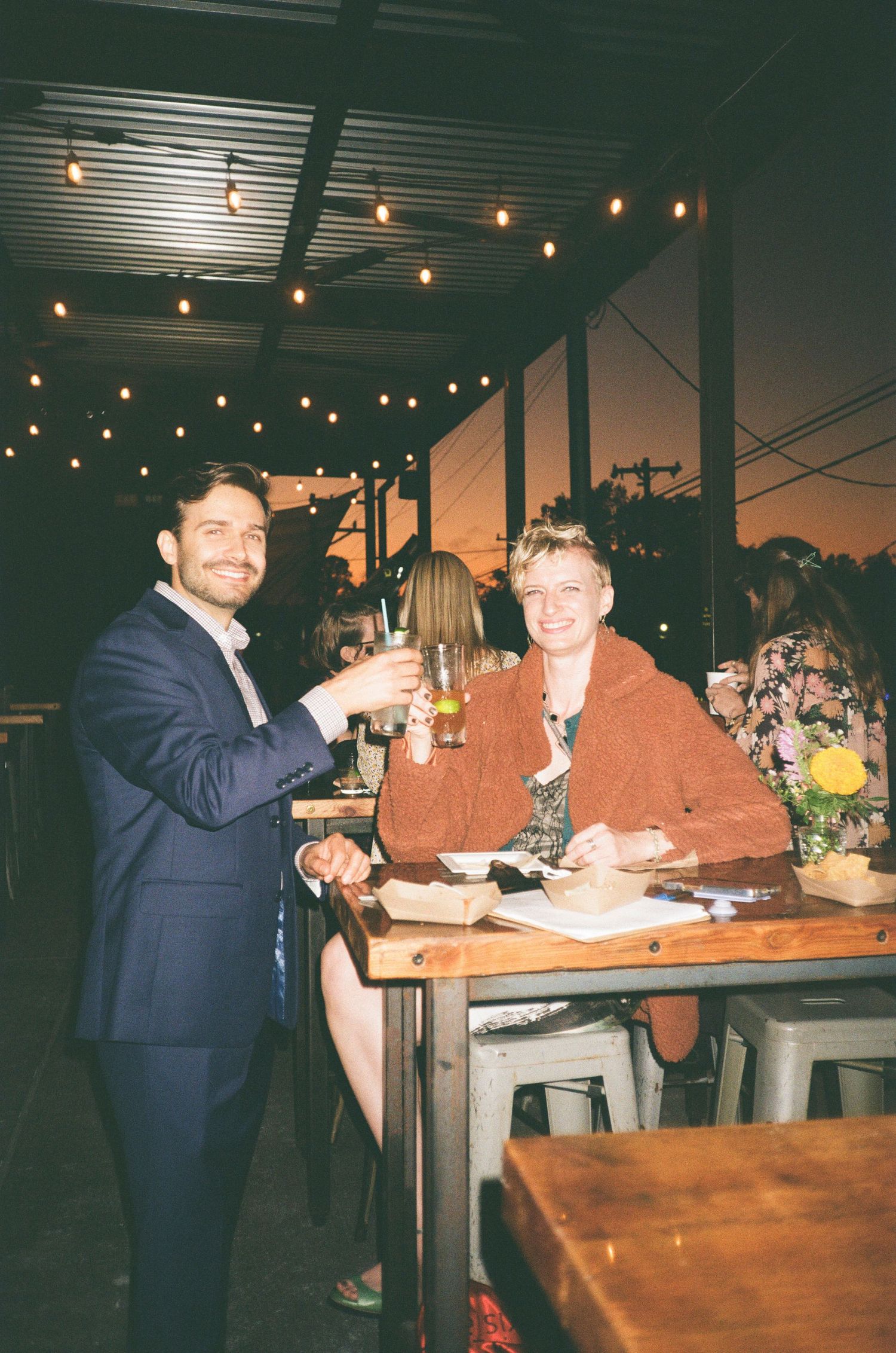 Evening reception under string lights with guests enjoying dinner and drinks at sunset.