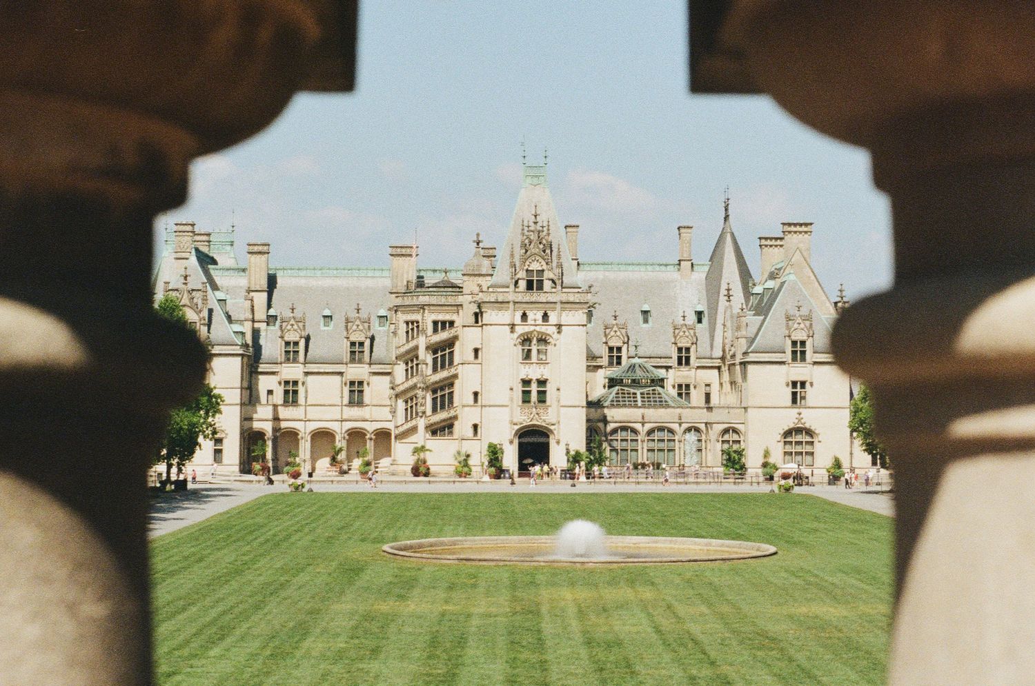 View of Biltmore Estate mansion through stone archway with manicured lawn in foreground in Asheville, North Carolina.