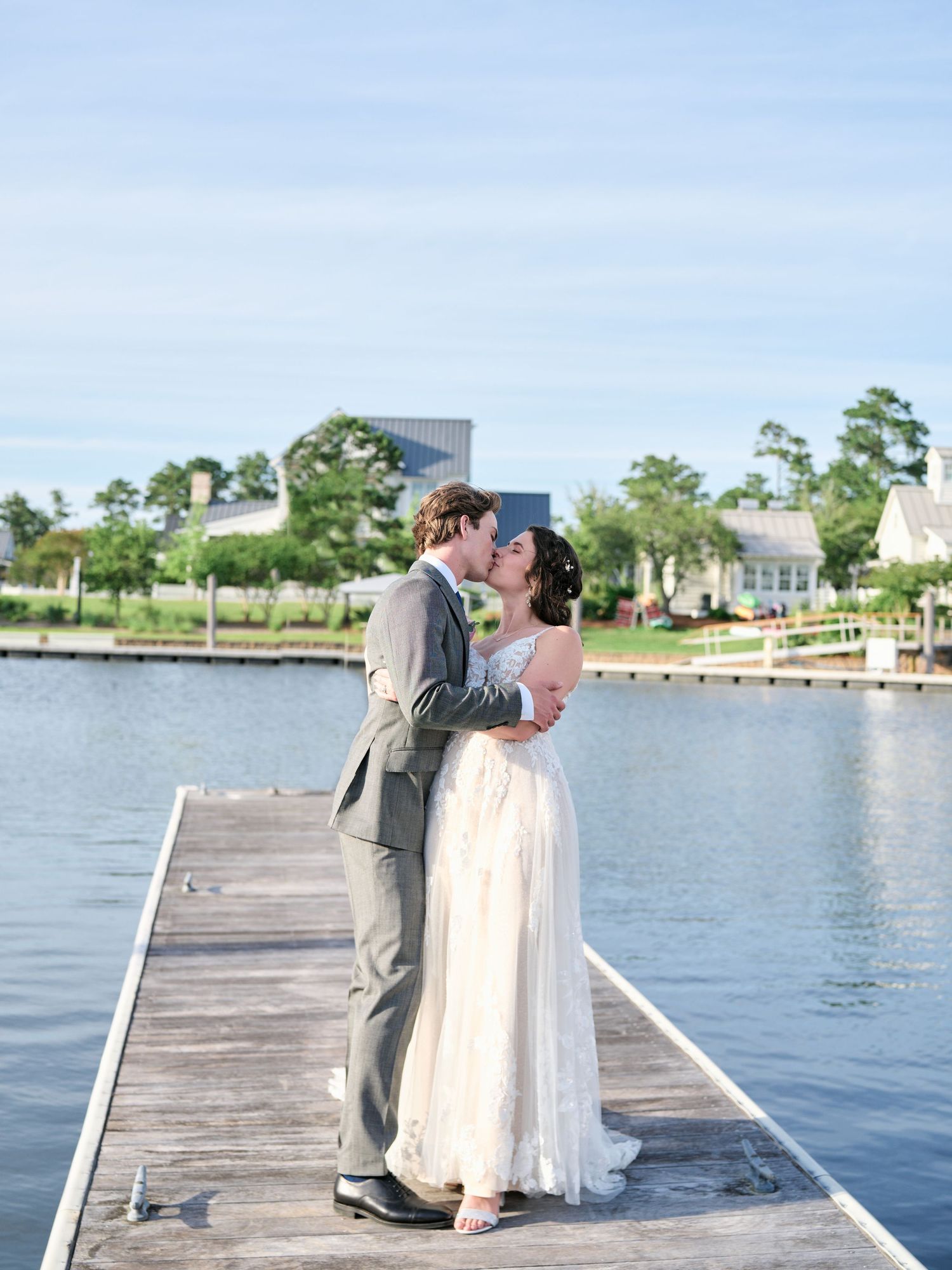 A romantic moment shared between a couple in wedding attire standing on a wooden dock overlooking a serene waterfront.