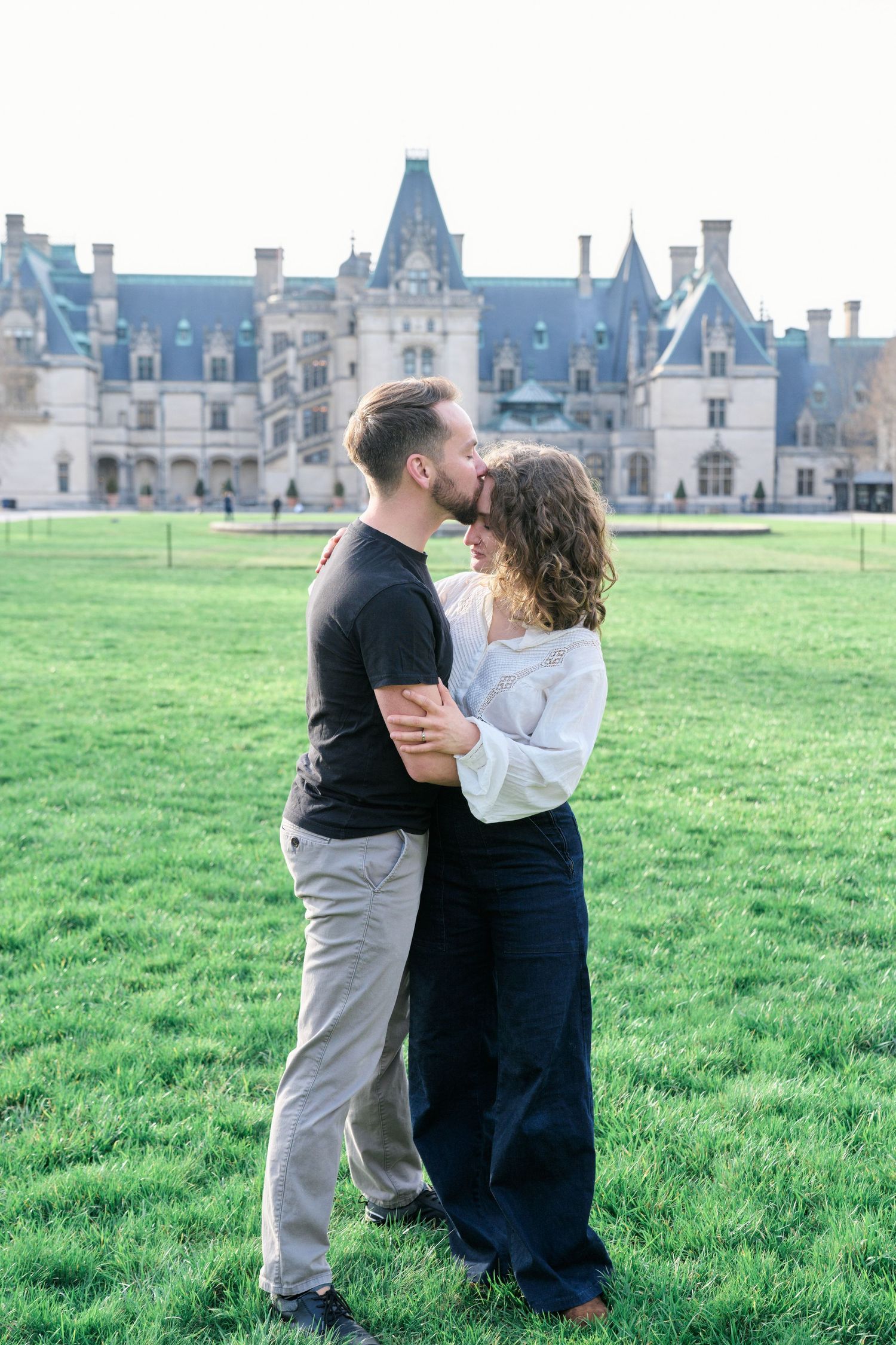 Intimate portrait of couple standing on the lawn with Biltmore Estate mansion in background.