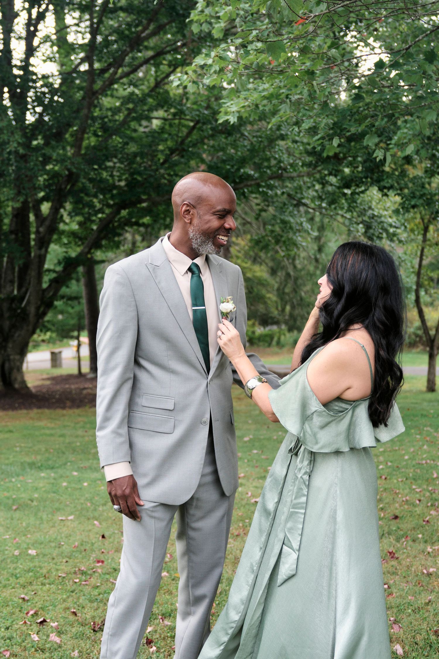 A couple in formal attire shares a joyful moment on a grassy lawn.