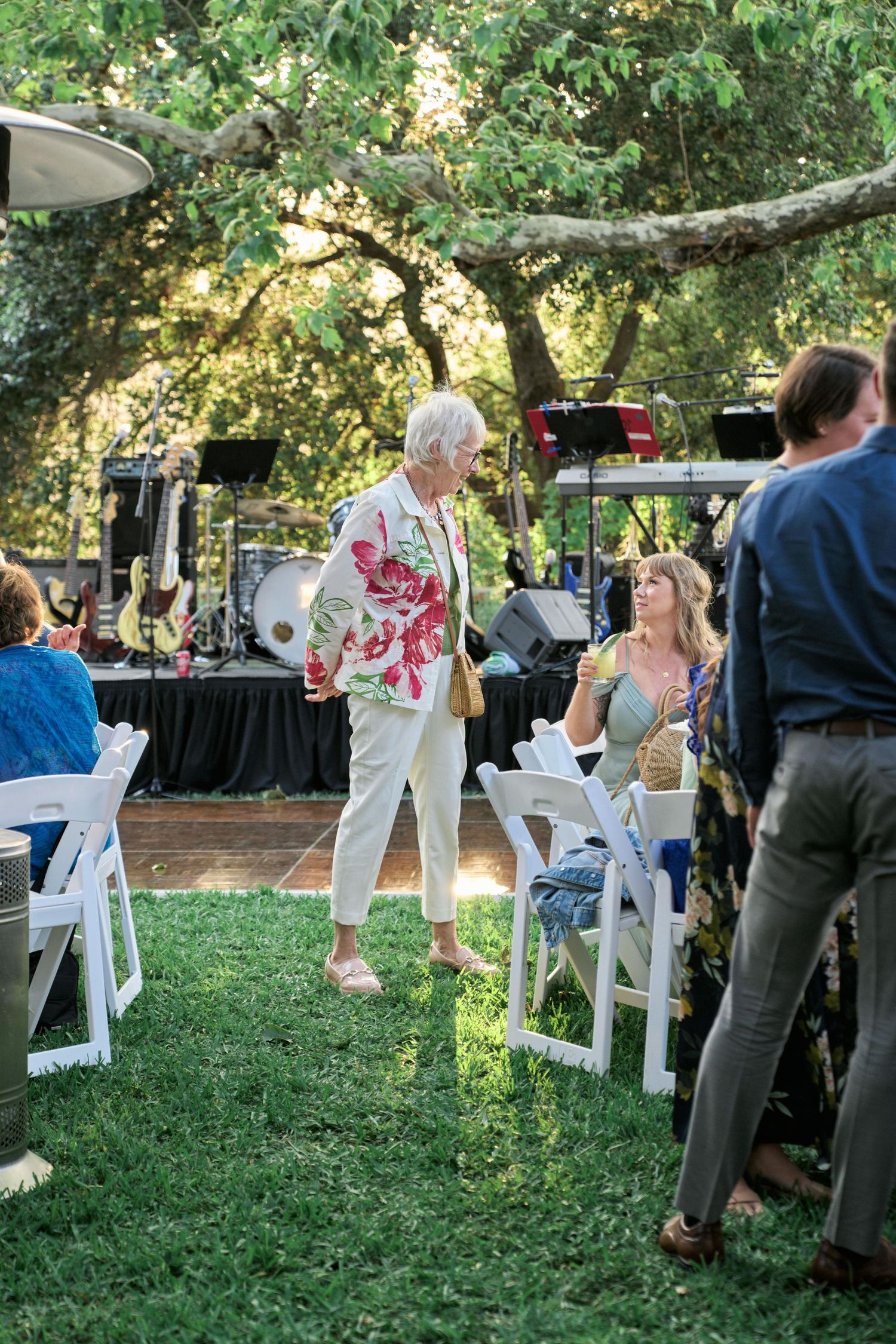 Lively outdoor wedding reception with live music and dancing under trees.