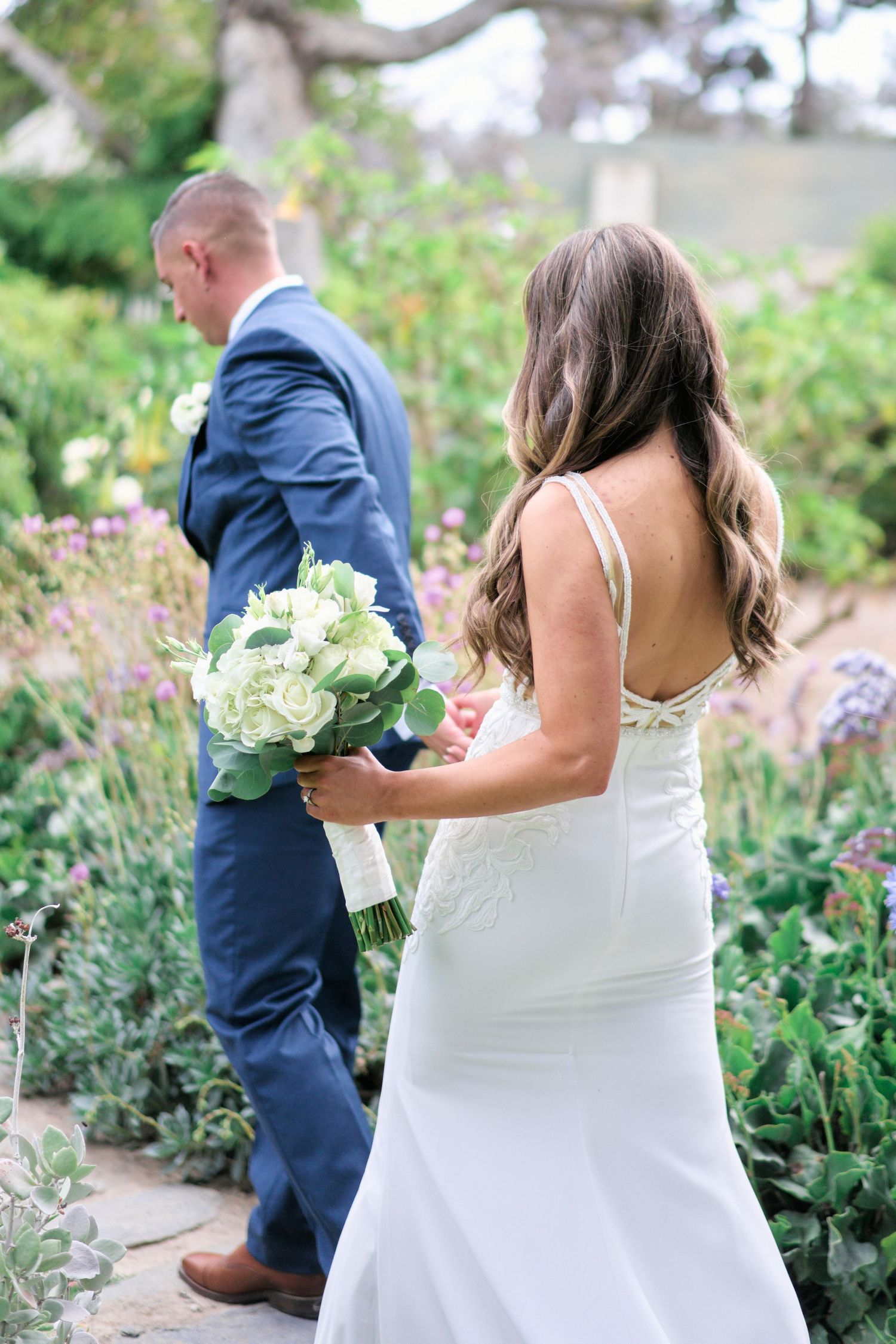 Elegant wedding couple in garden setting with bride holding white bouquet.