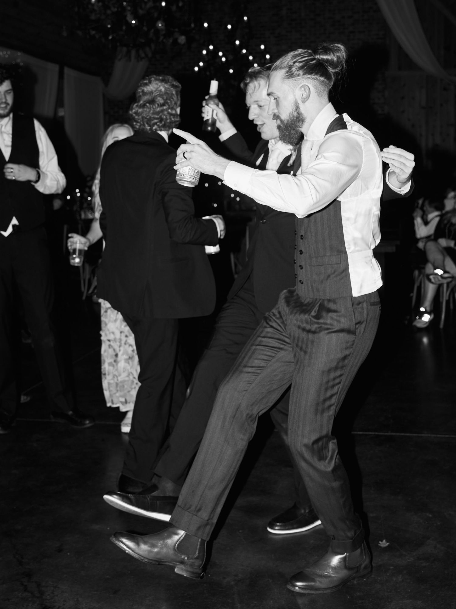 Black and white photo of wedding reception dancing with string lights overhead.