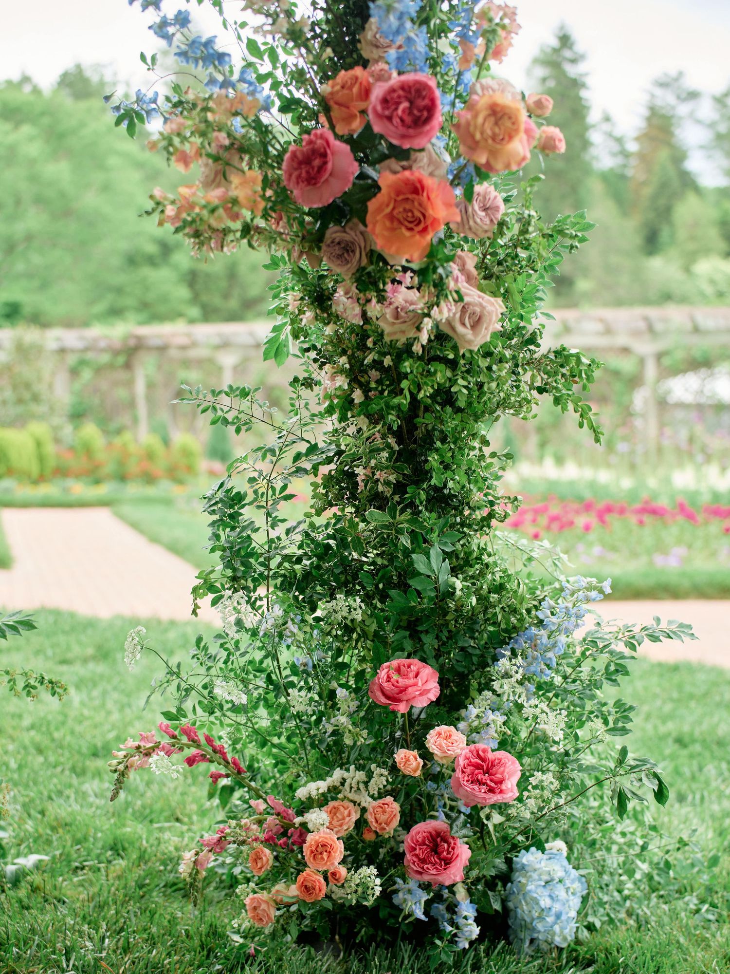 Elegant floral arrangement featuring coral and pink roses with delicate greenery in an outdoor garden setting.