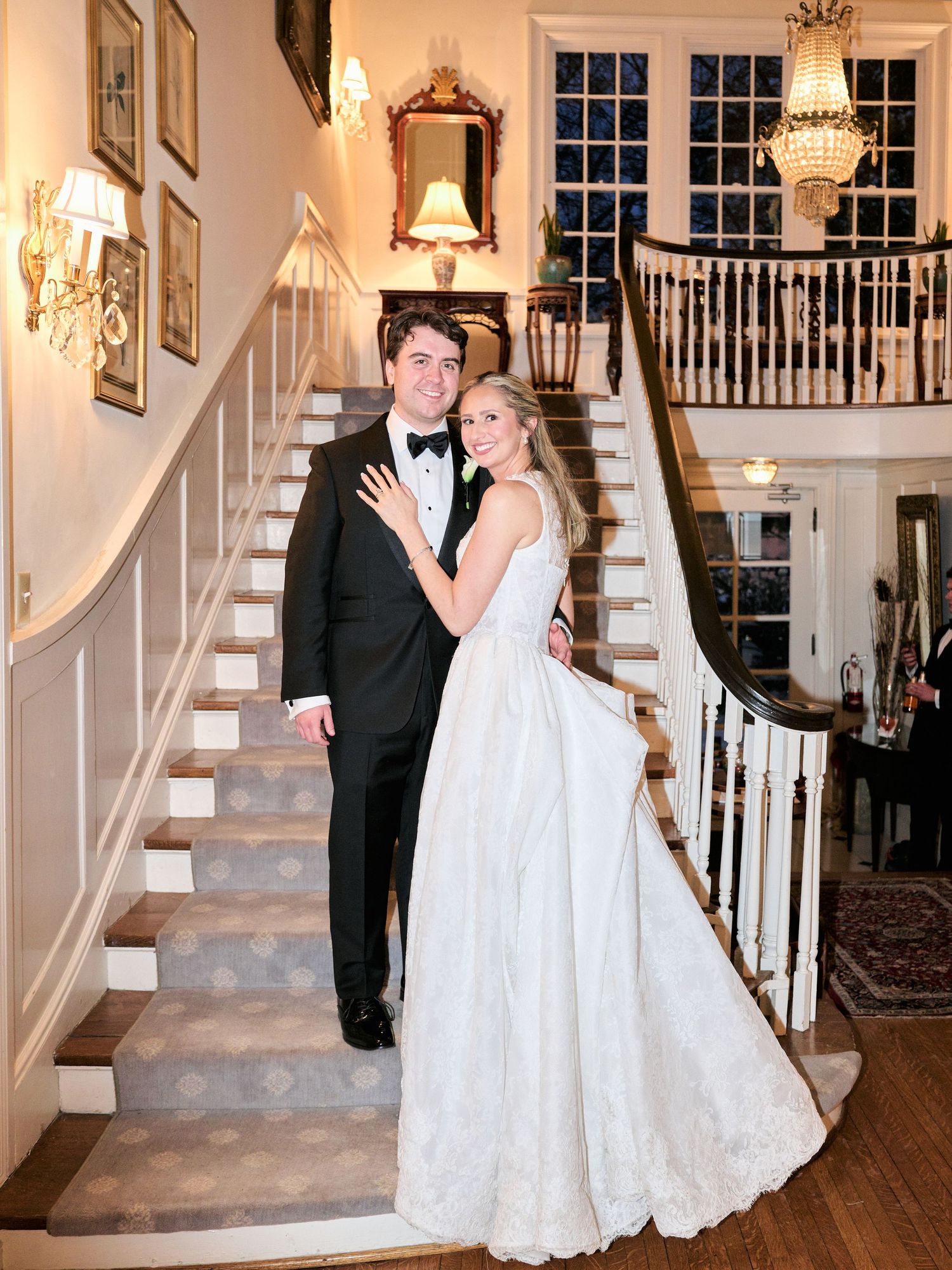 Bride and groom pose elegantly on grand staircase in classic wedding attire at upscale venue.