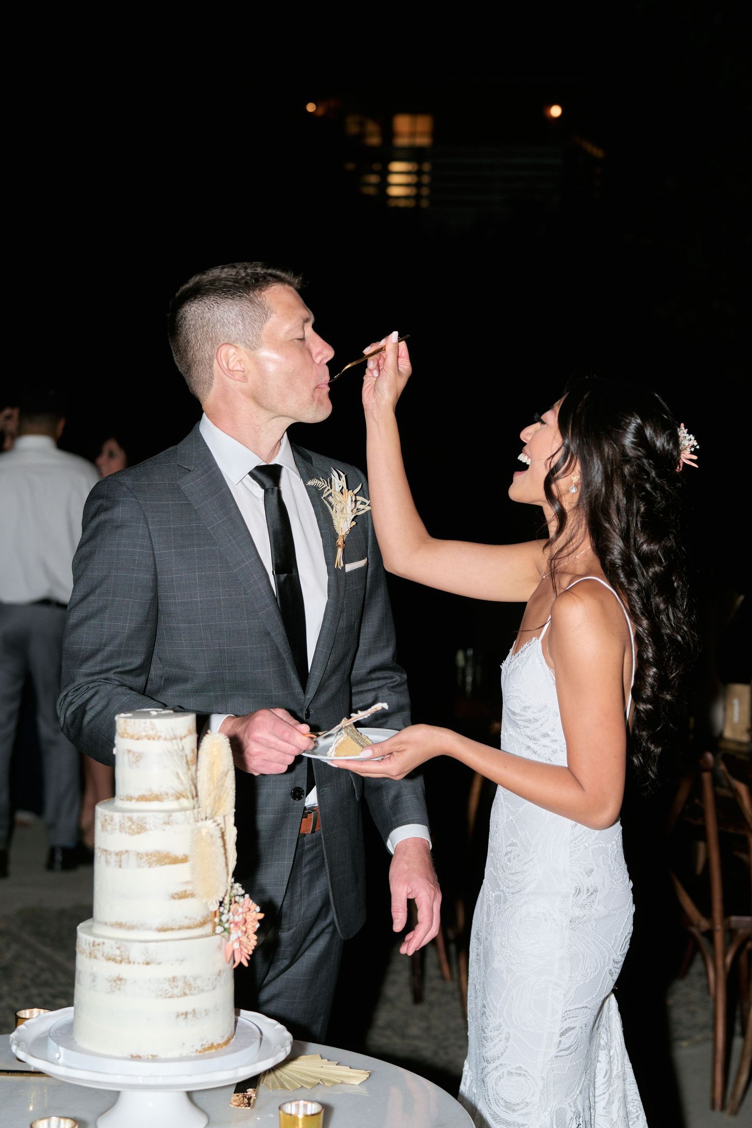 Bride playfully feeds wedding cake to groom during their reception celebration.