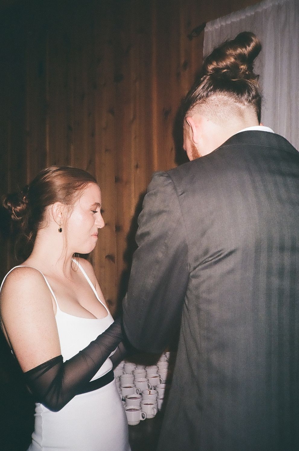 A couple shares an intimate moment during a wedding, with the bride wearing a white dress and long black gloves.