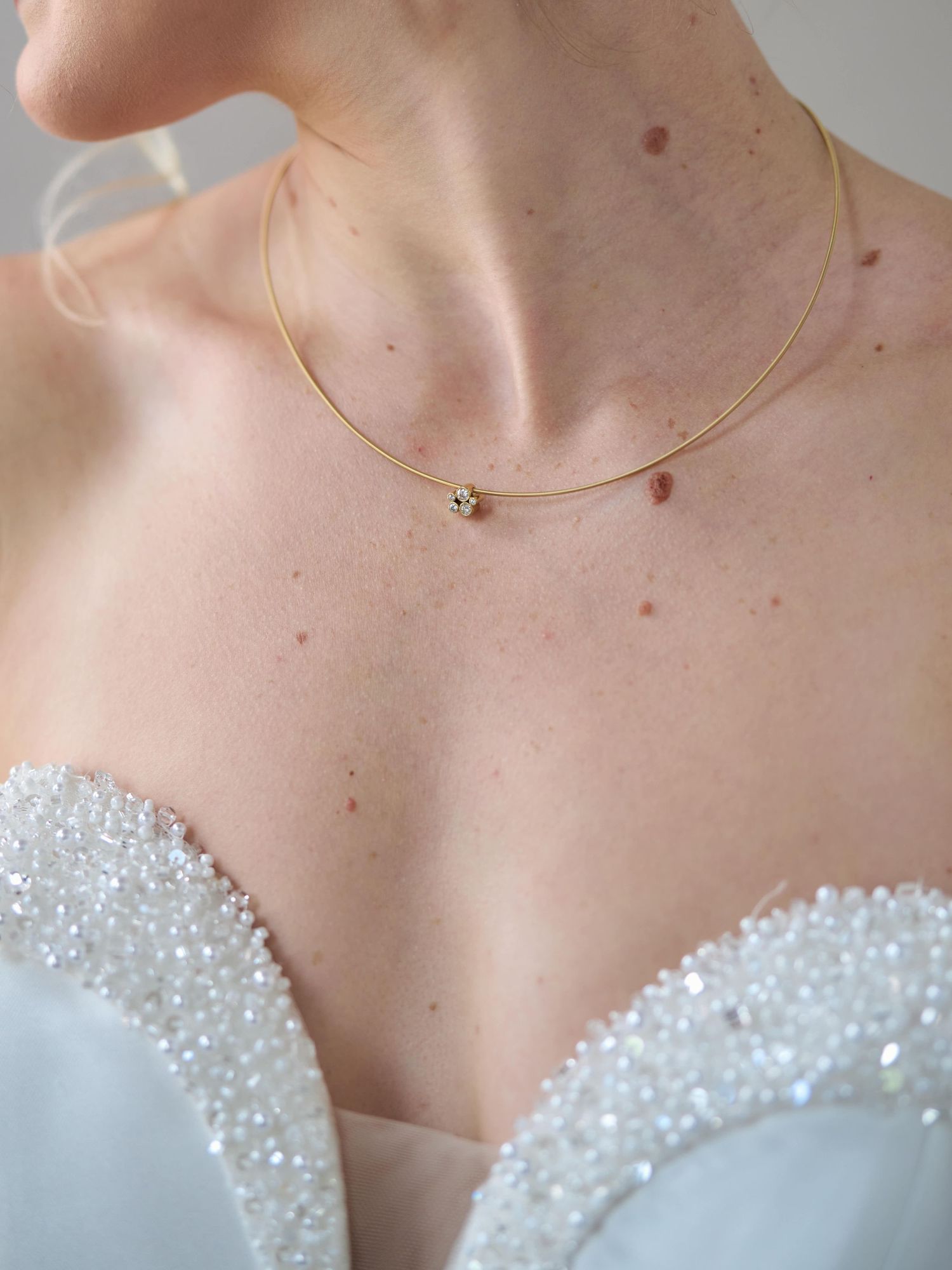 Close-up of delicate gold necklace with crystal detail on beaded wedding dress bodice.
