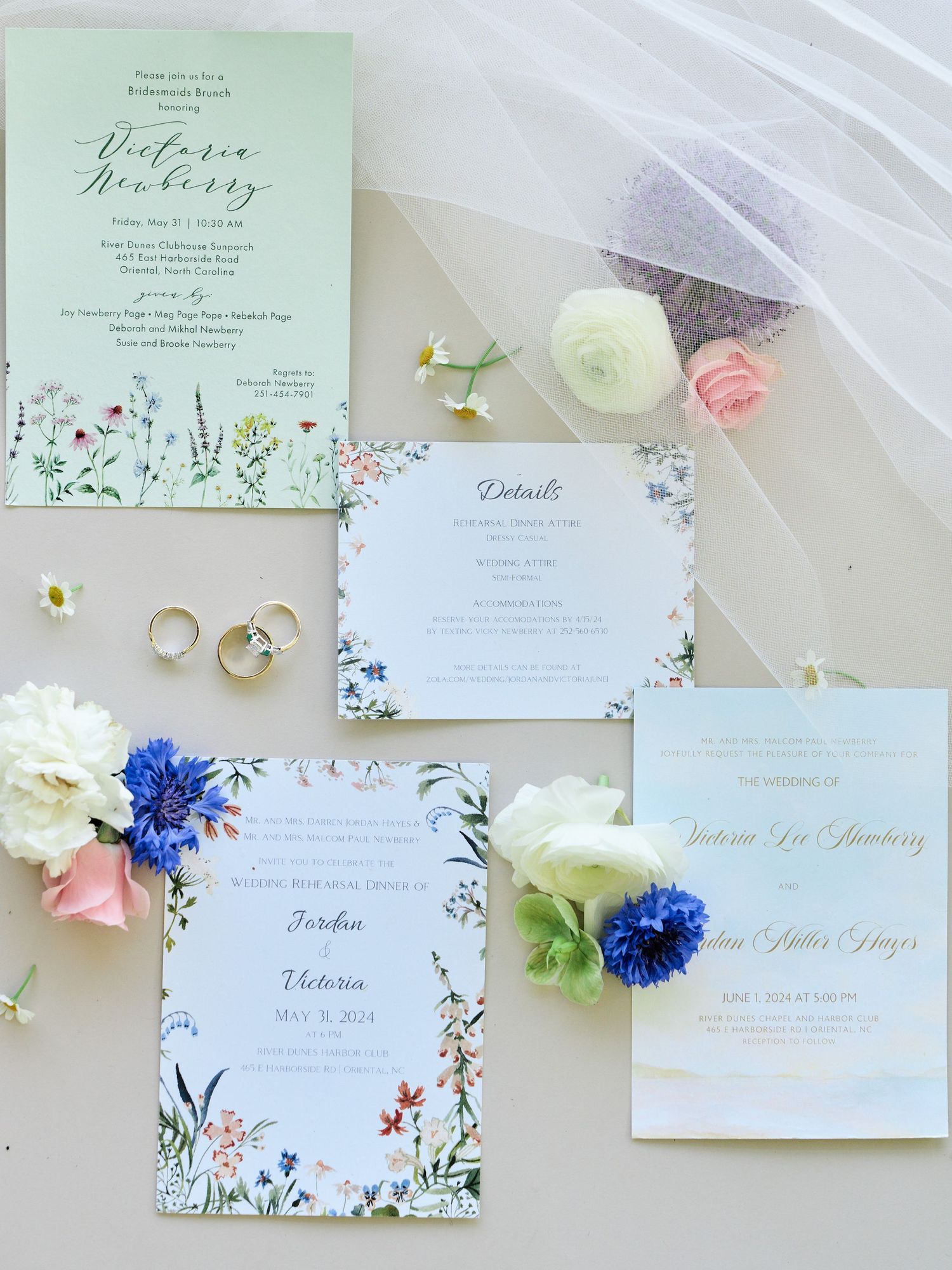 Elegant floral wedding invitation suite with pink and blue flowers, gold rings, and delicate stationery on light background.