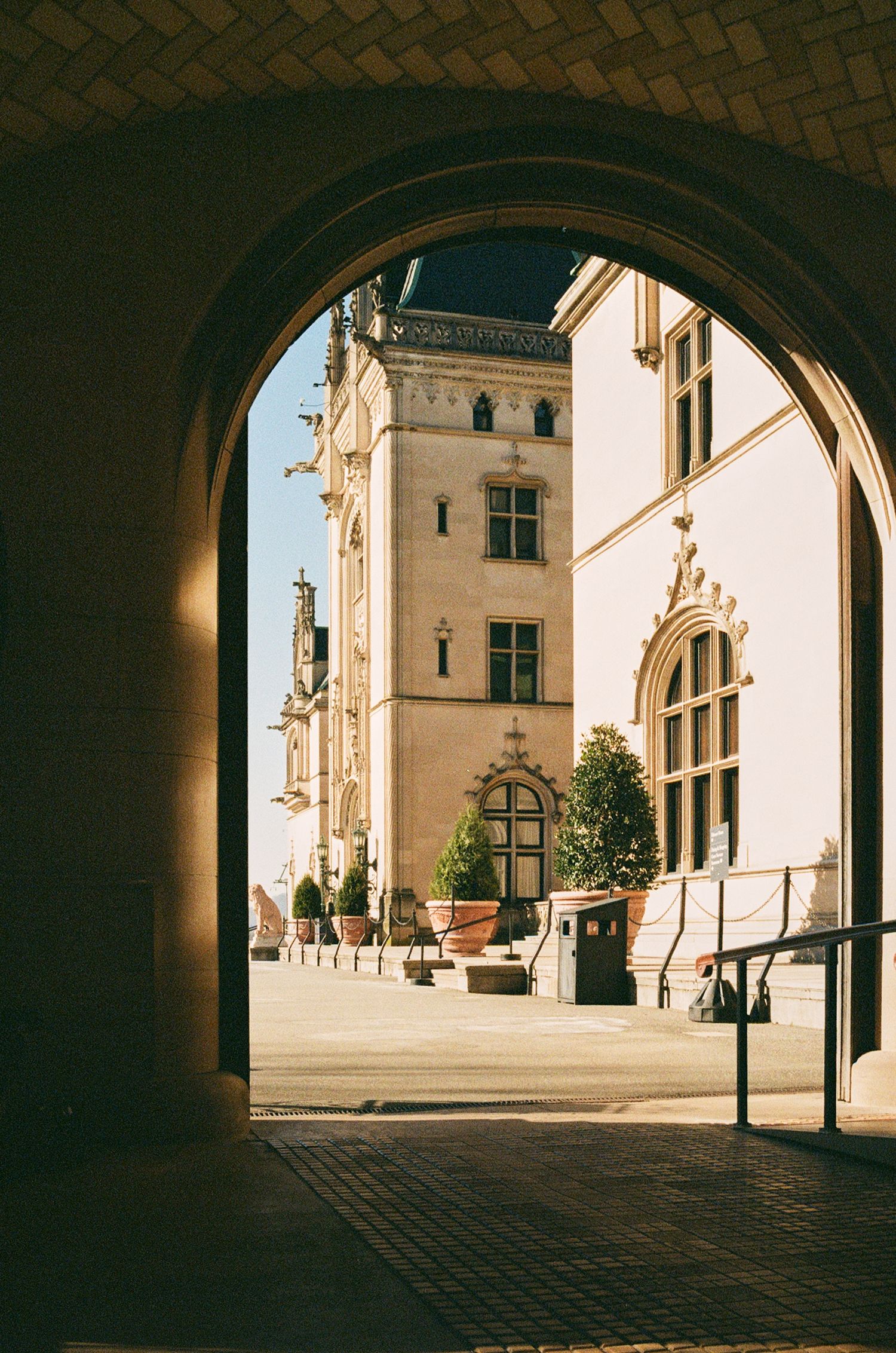 View through stone archway of historic European building with white facade and ornate architectural details in sunlight.