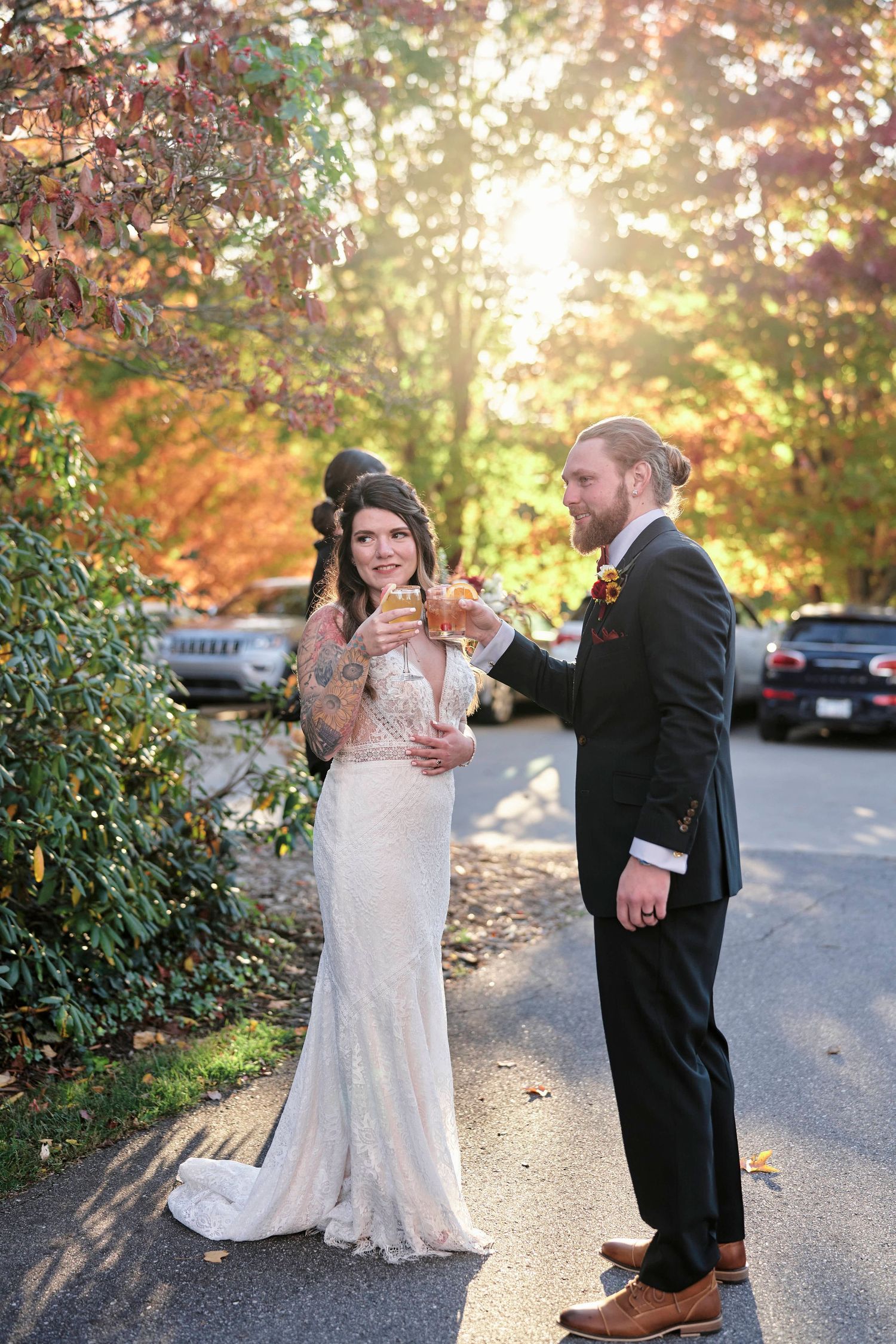 A couple shares a toast outdoors during golden hour surrounded by fall foliage.